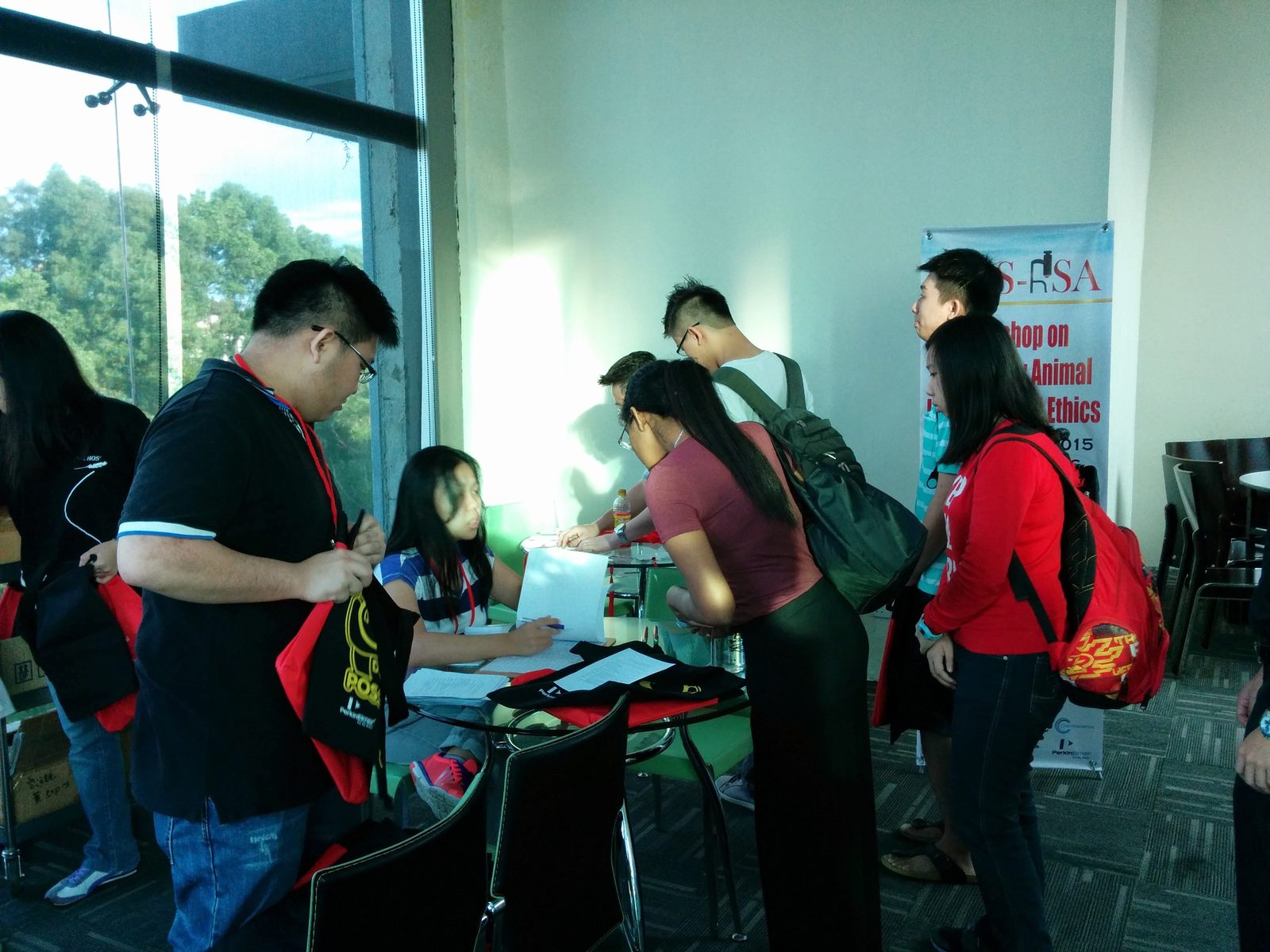 Participants sign in at the registration table, holding red workshop bags, with the workshop banner standing behind them