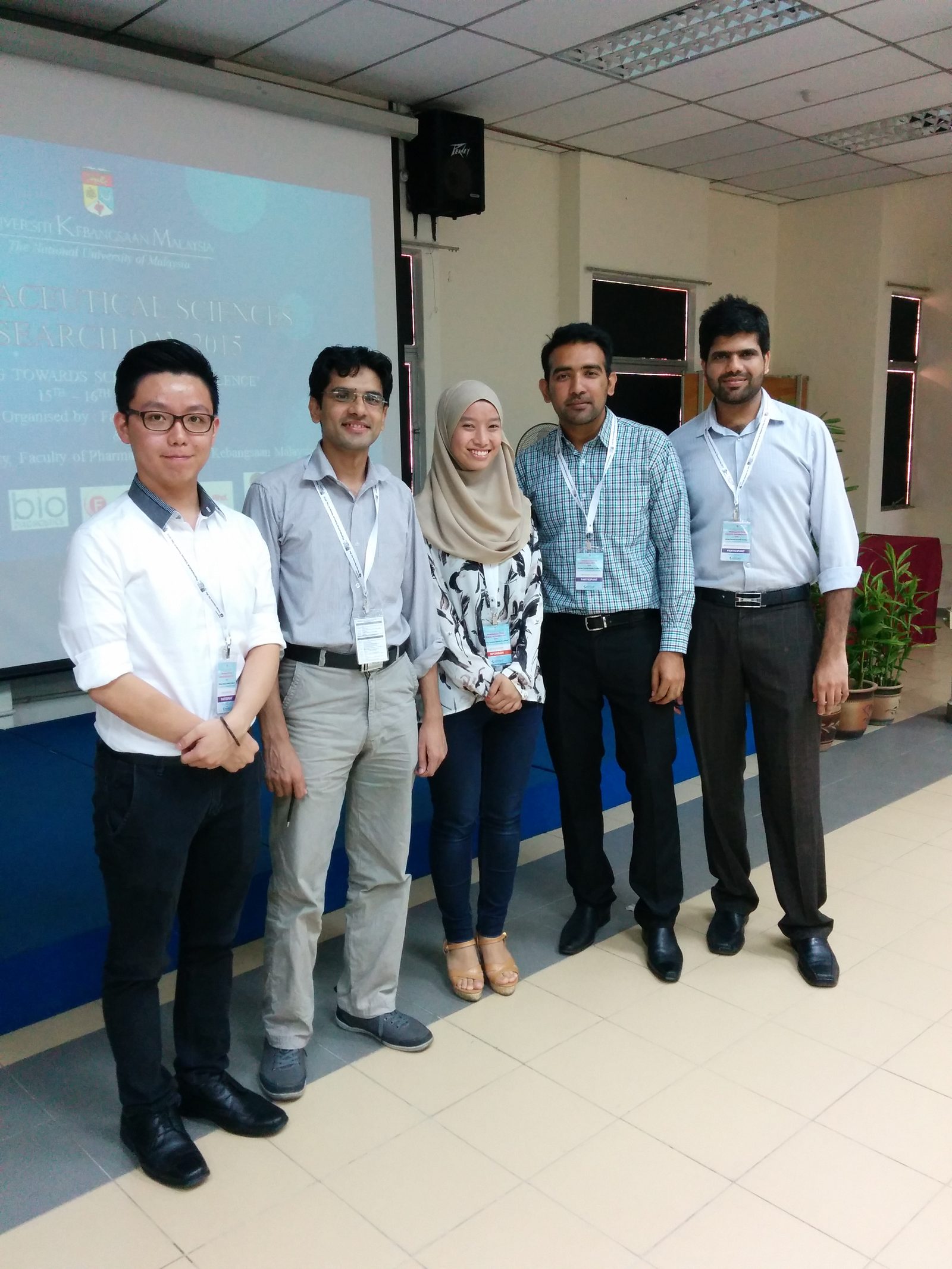 Five people wearing name tags standing in front of the research day's title slide