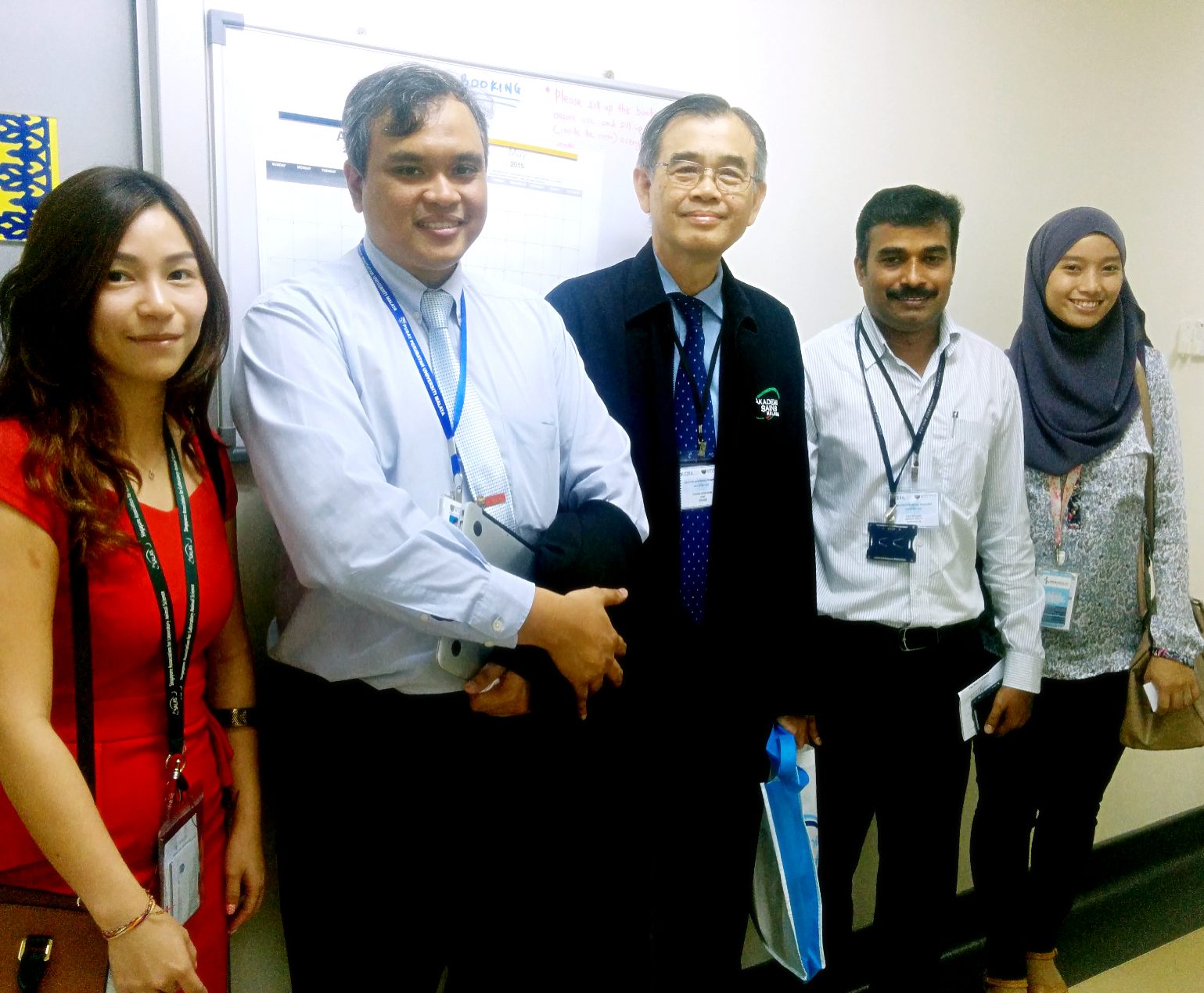 Five people wearing event name badges stand together for a photo in a corridor