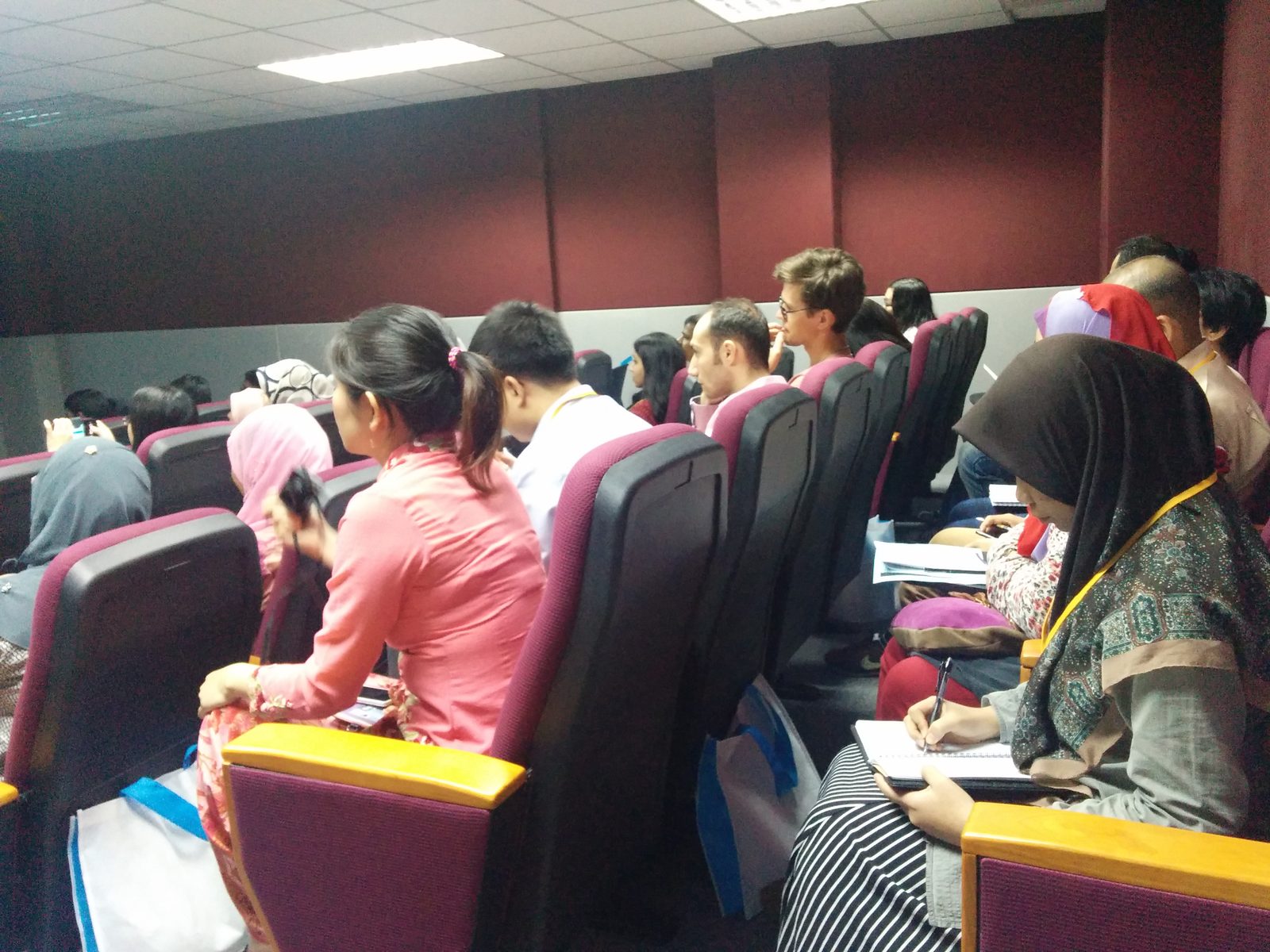 Seated participants in a lecture hall listen and take notes