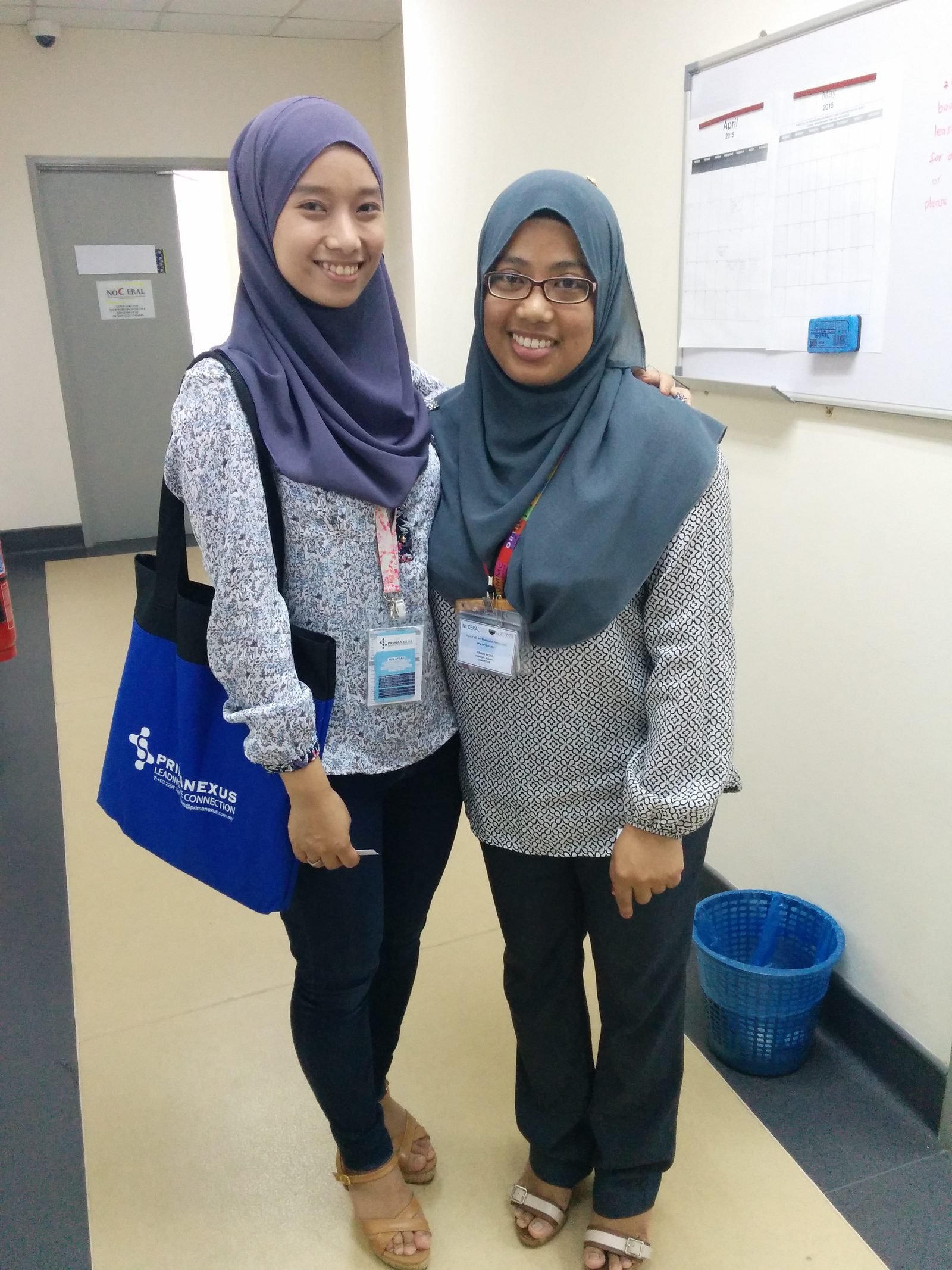 Two women with name badges stand in a corridor, one carrying a blue Prima Nexus bag