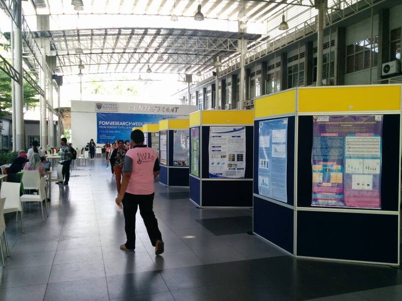 Research posters on yellow and navy display panels along a covered walkway, with the event banner behind