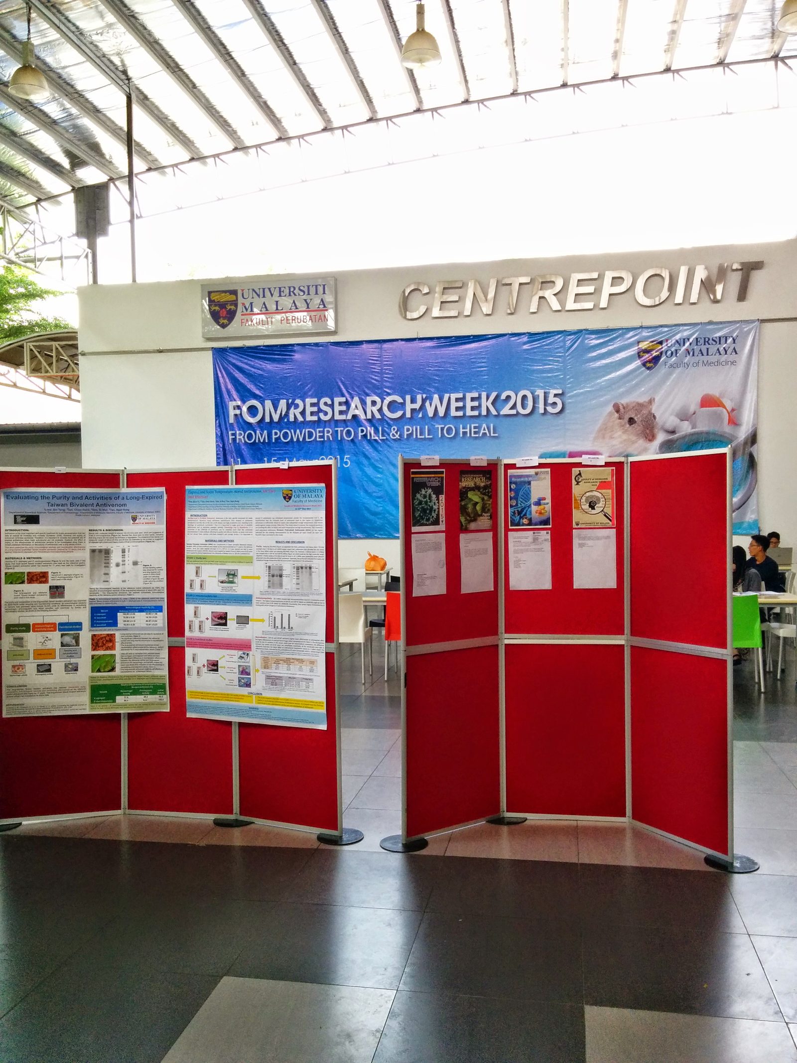 Red display boards with research posters beneath the FOM Research Week 2015 banner at Centrepoint