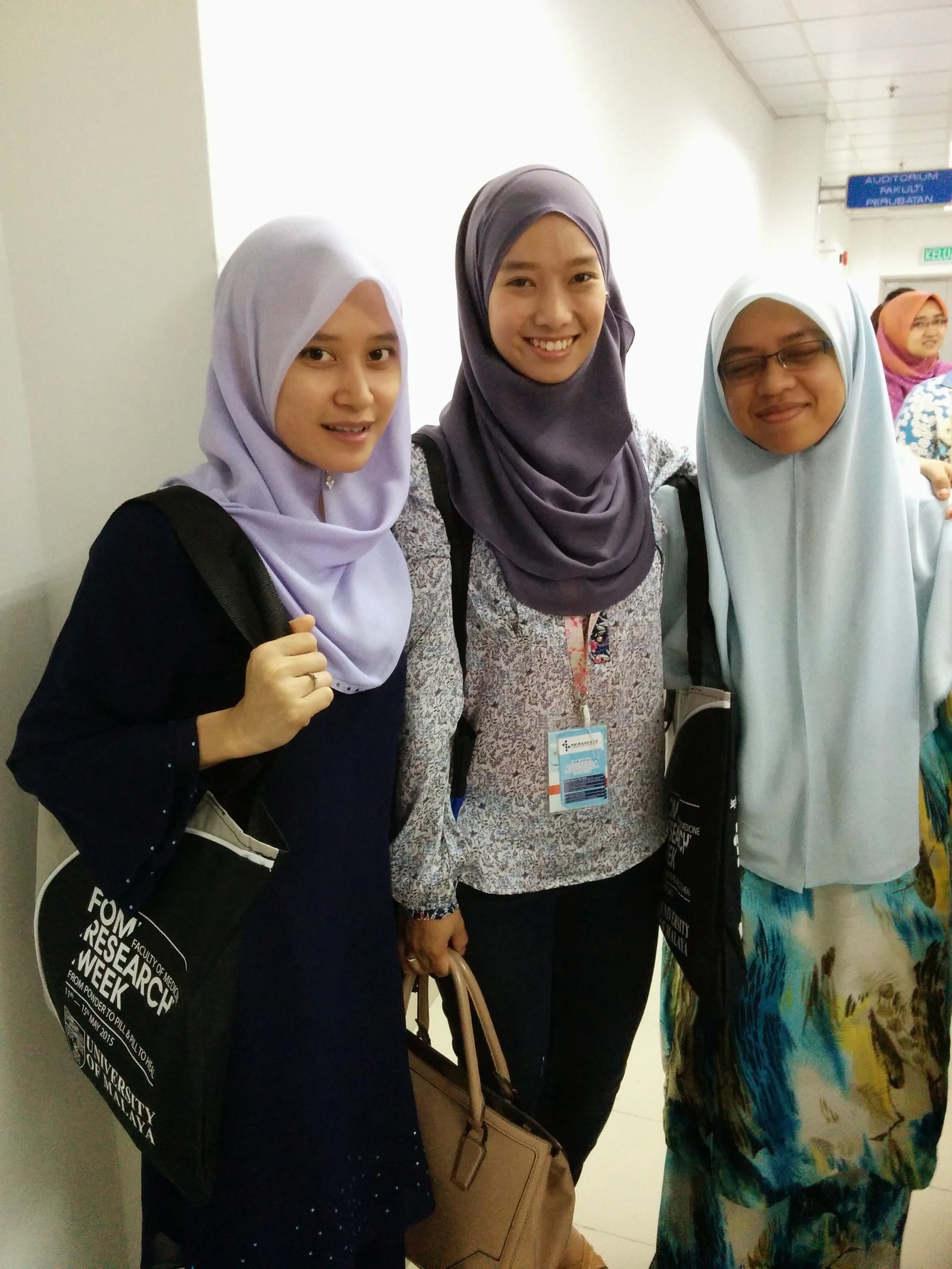 Three women in a corridor, one carrying a black FOM Research Week tote bag