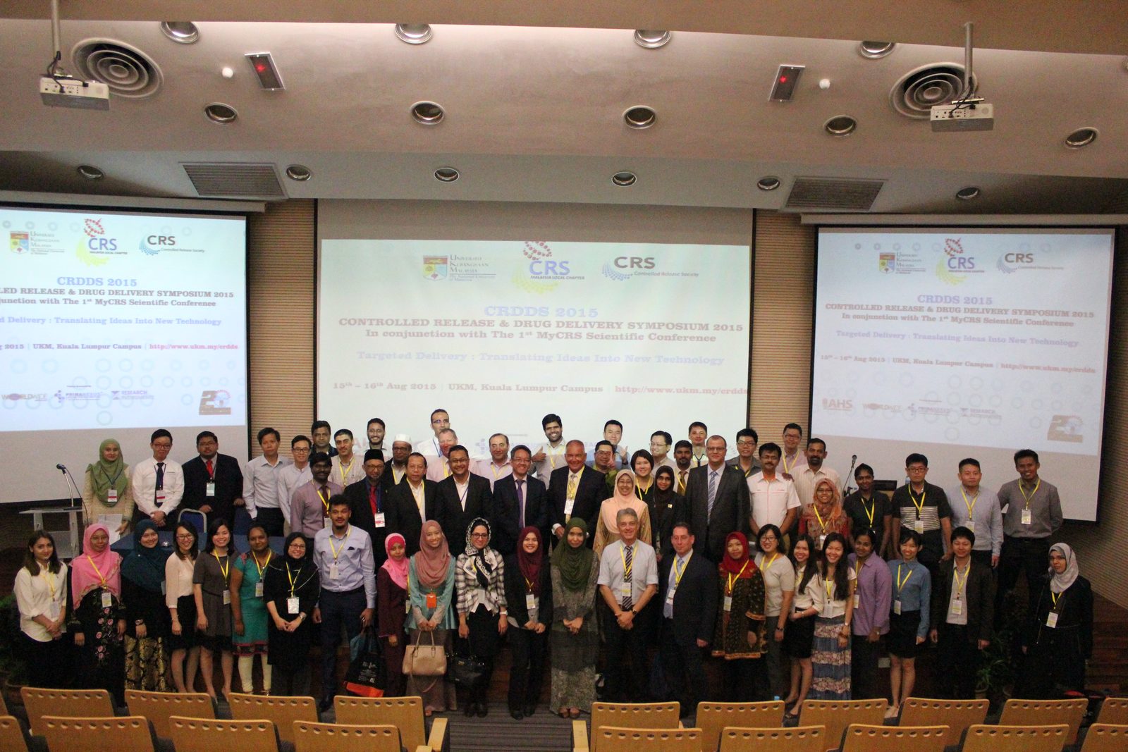 Delegates of CRDDS2015 pose for a group photo in a lecture hall, with the symposium title on three screens