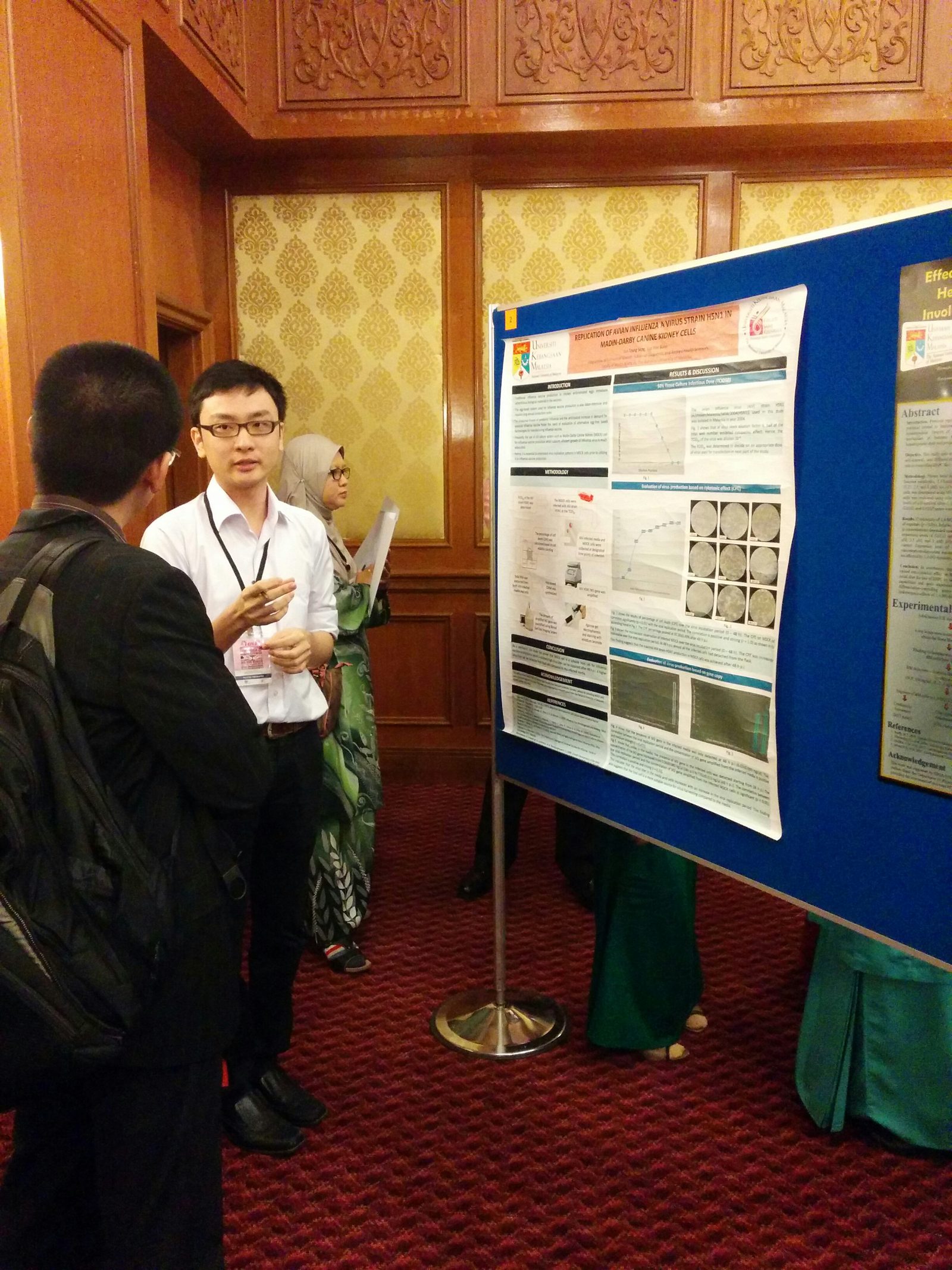 A poster presenter explains his research poster to a delegate beside a blue poster board