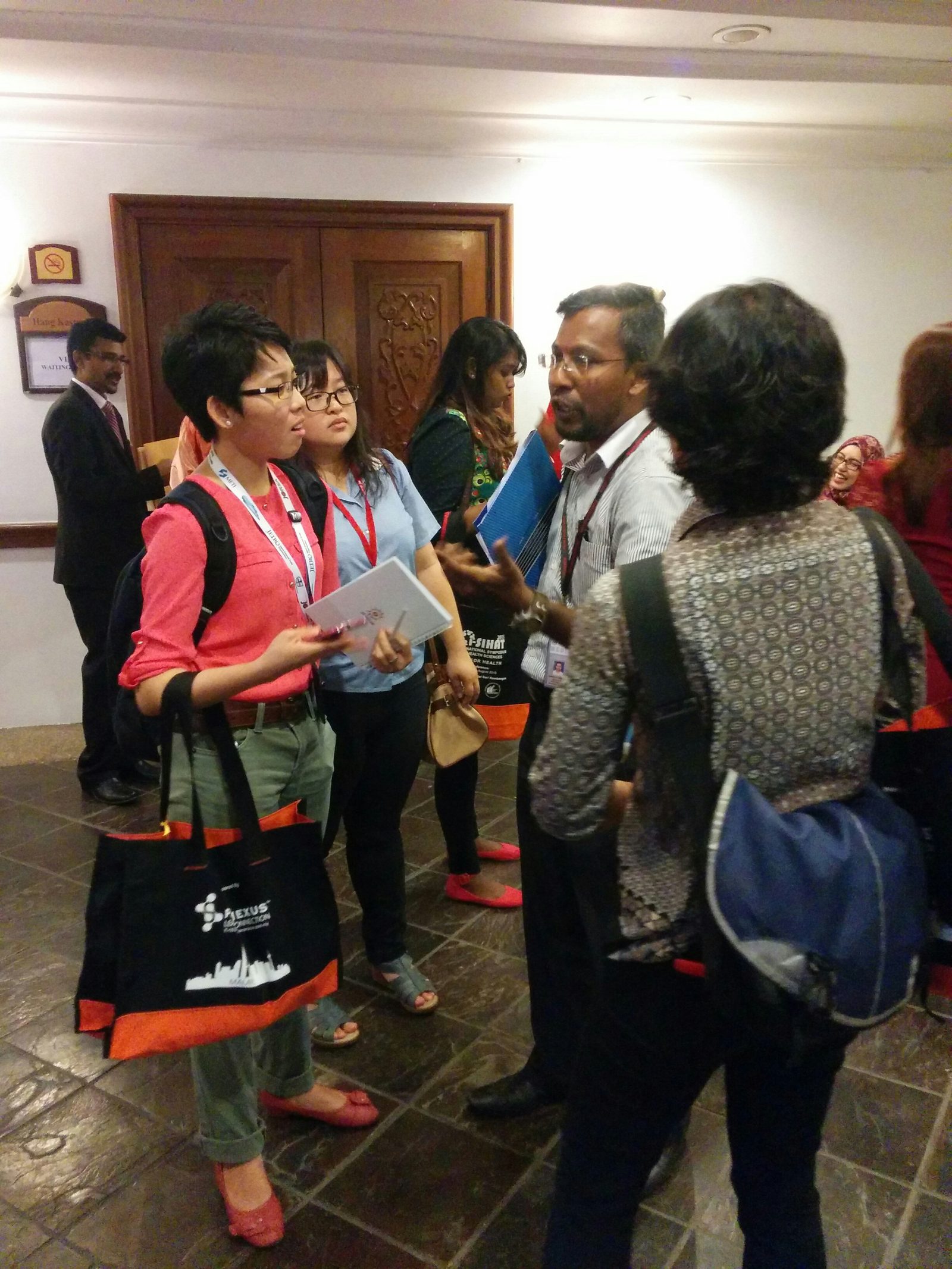 Delegates carrying black and orange i-SIHAT bags talk together in the hotel corridor