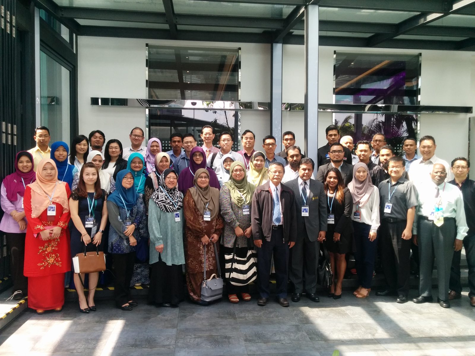 Group photo of the seminar participants standing in rows under a glass canopy at Le Meridien Kuala Lumpur