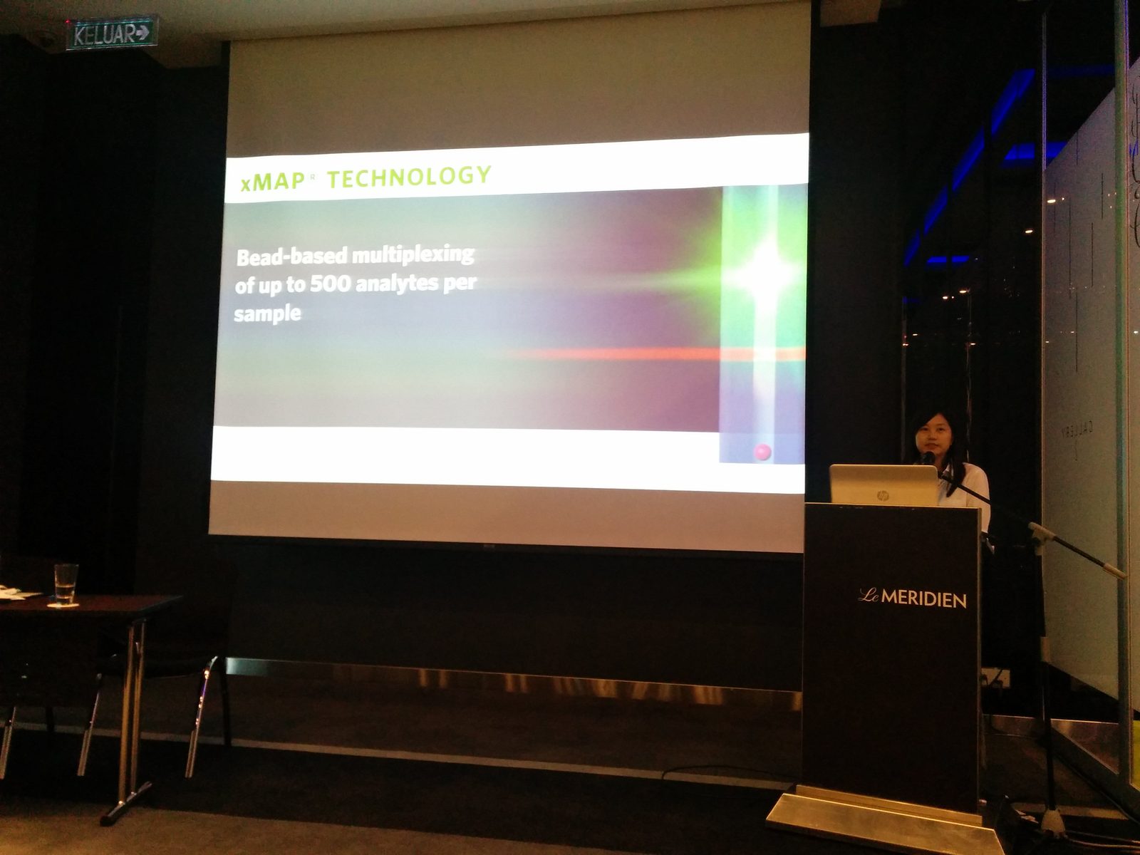 A speaker at the lectern beside a slide titled xMAP Technology, bead-based multiplexing