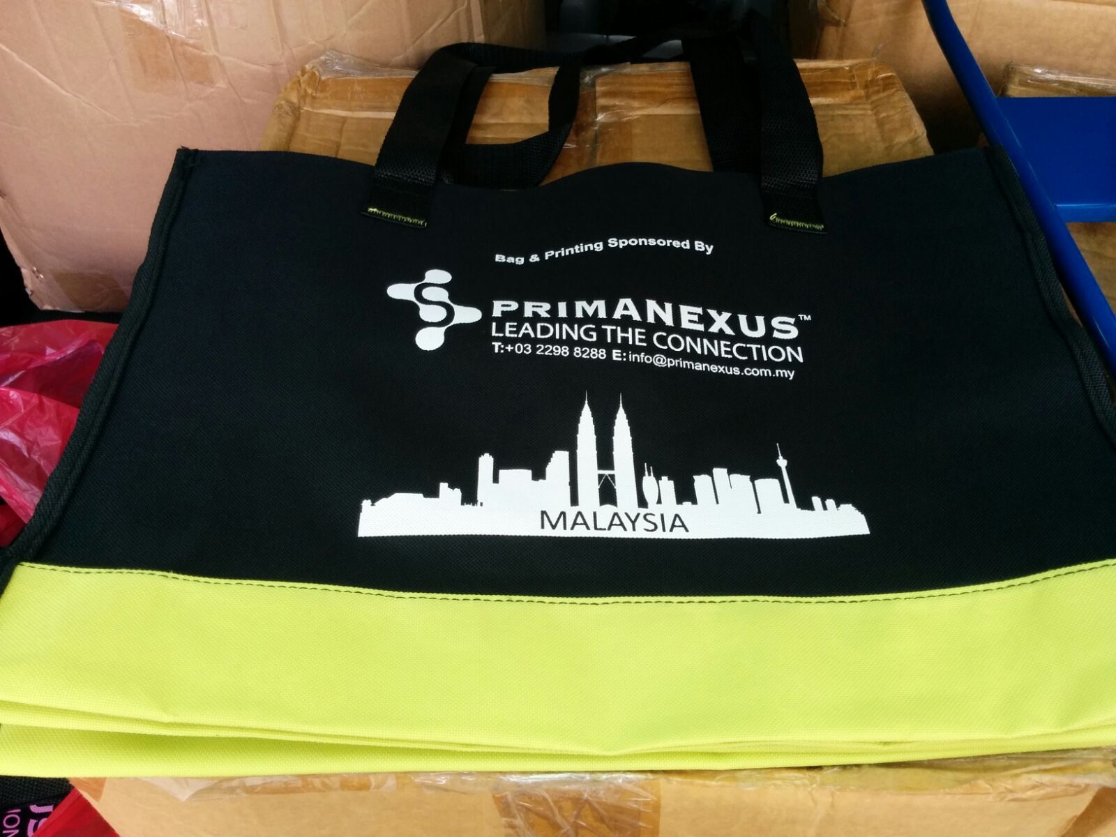A black and lime seminar bag printed with the Prima Nexus logo and a city skyline labelled Malaysia