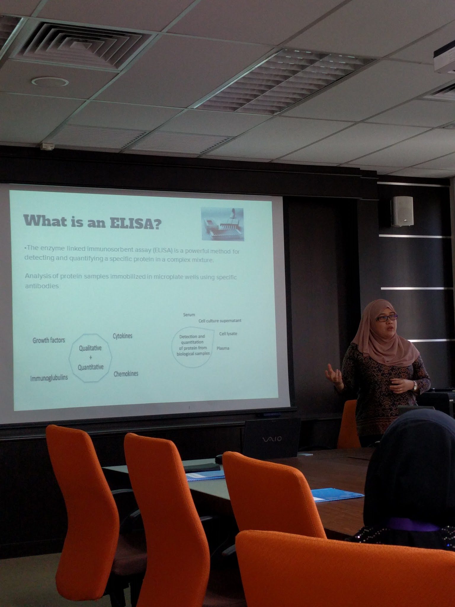 A trainer presents a slide titled What is an ELISA? to the seminar room