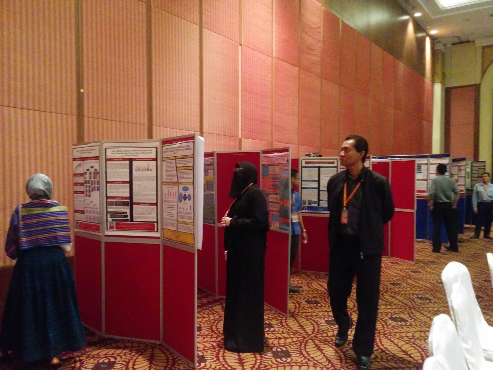 Delegates reading research posters mounted on red display boards in the conference hall