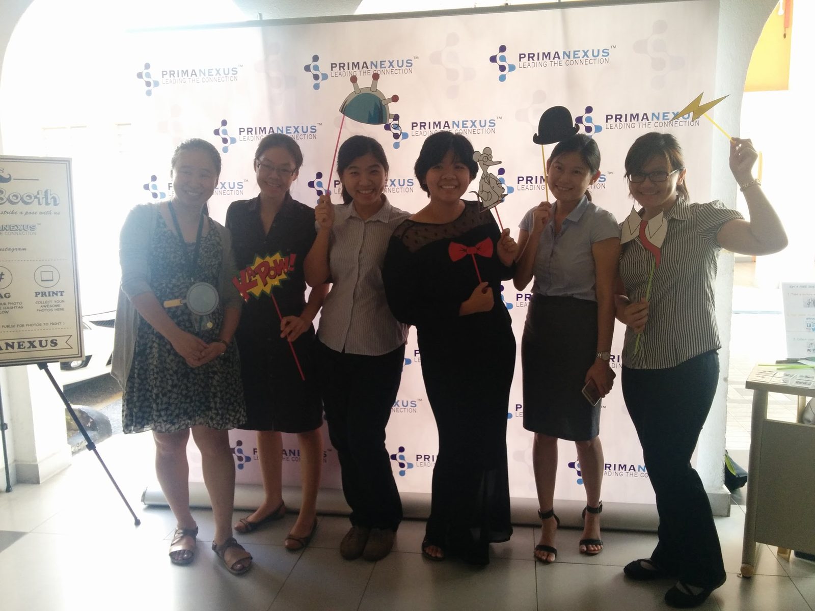 Six people holding photo props in front of the Prima Nexus logo backdrop