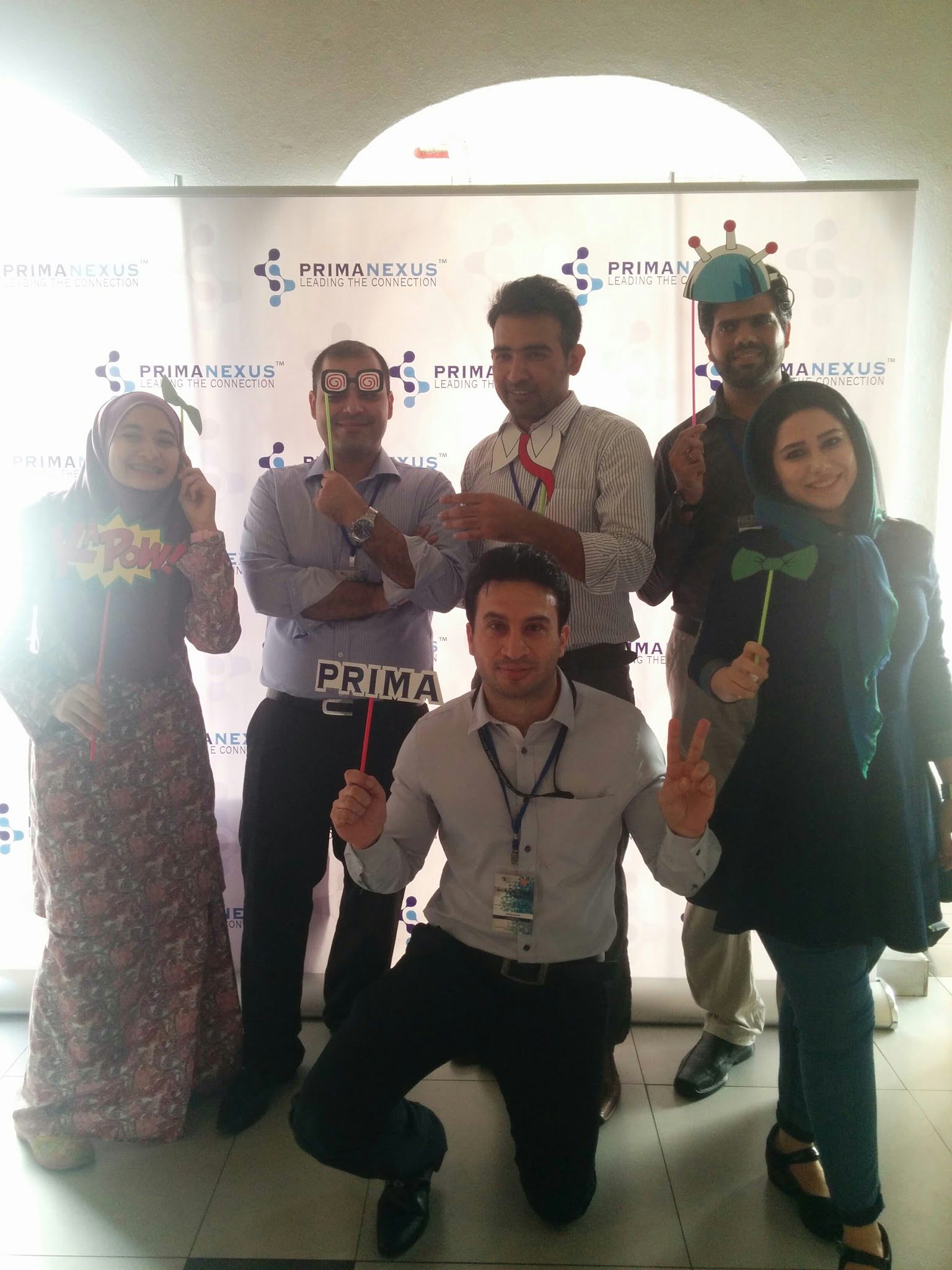 Six people posing with props, including a PRIMA sign, in front of the Prima Nexus backdrop