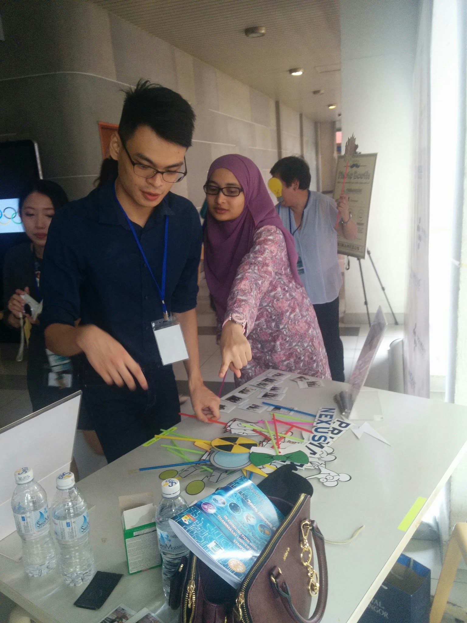 Two people at the booth table looking at printed photos and props, with the Prima Nexus backdrop behind
