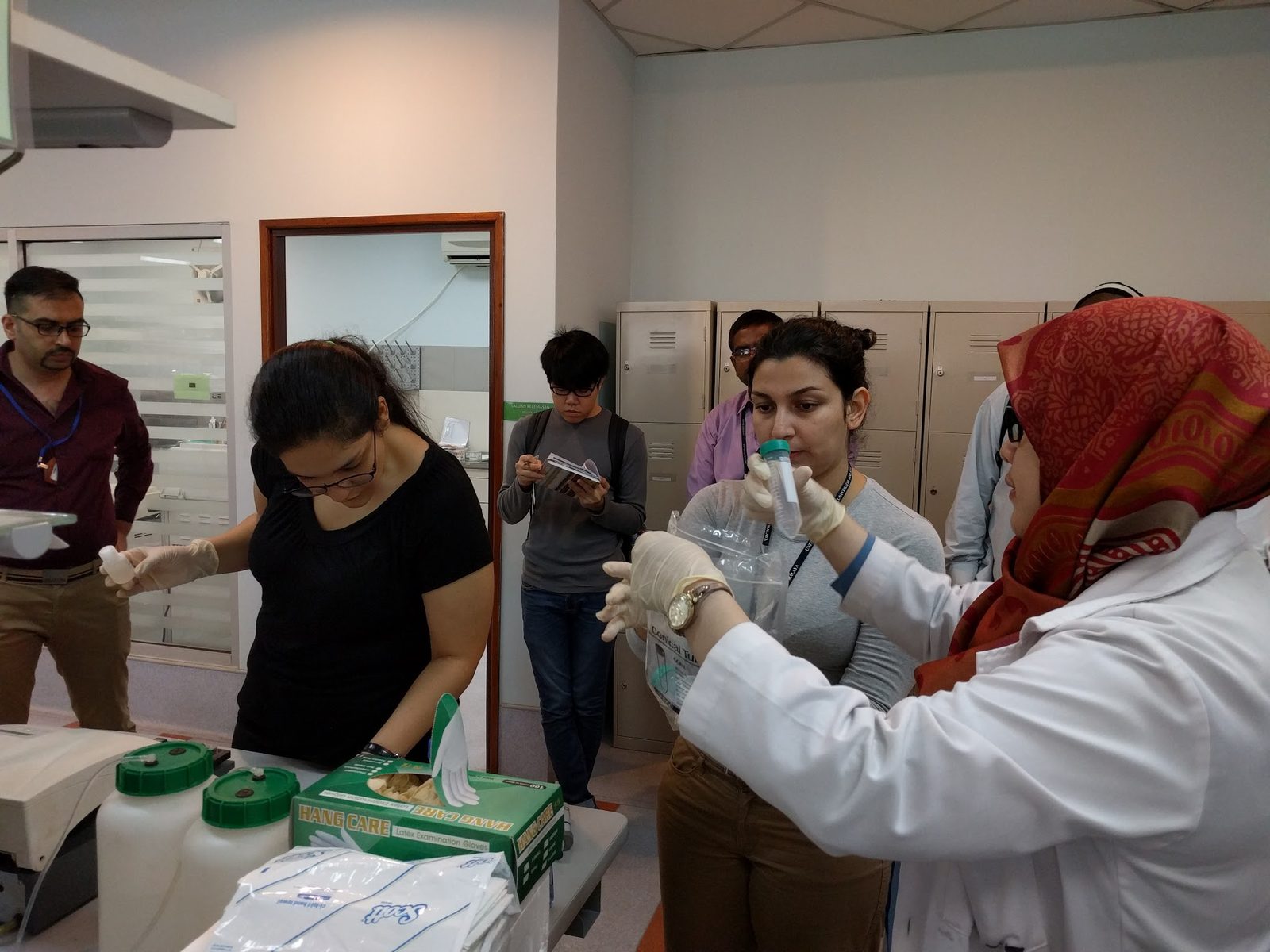 Participants in gloves handle tubes and reagent bottles at a laboratory bench