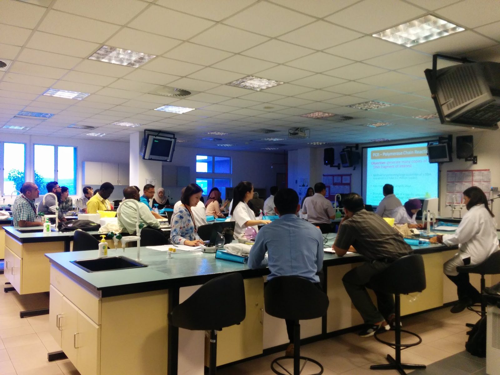A full teaching laboratory with participants seated at benches, facing a screen at the front