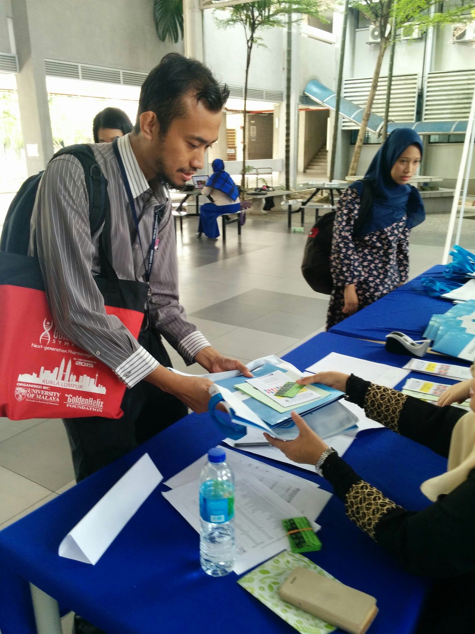 A participant receives a blue folder and papers from staff at the registration table