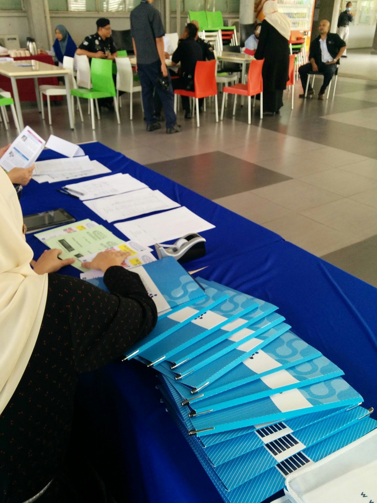 A fanned stack of blue Prima Nexus folders on the registration table, with a seating area behind