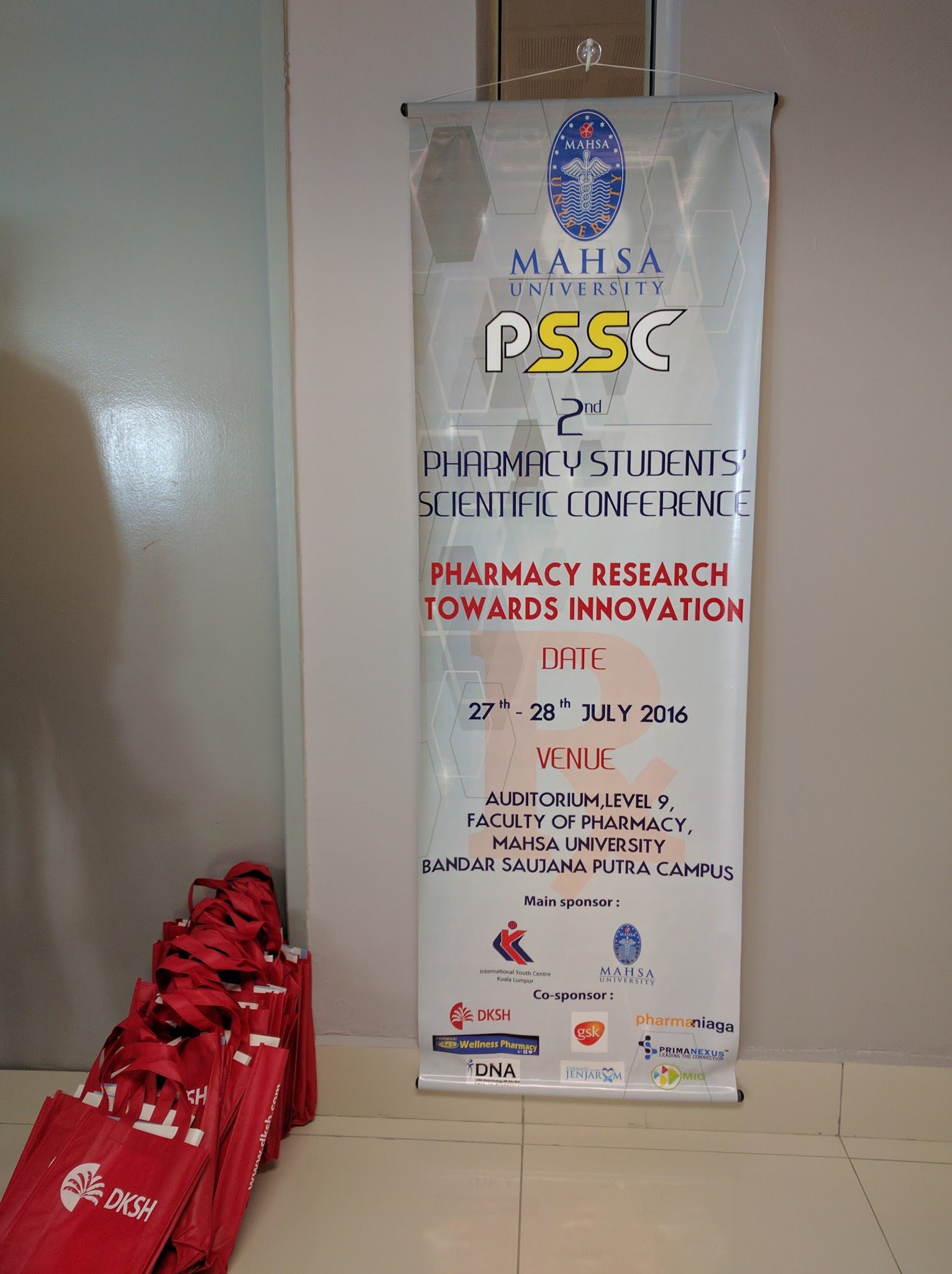 The conference banner standing in the venue, with sponsor logos at its foot, beside a stack of red bags.