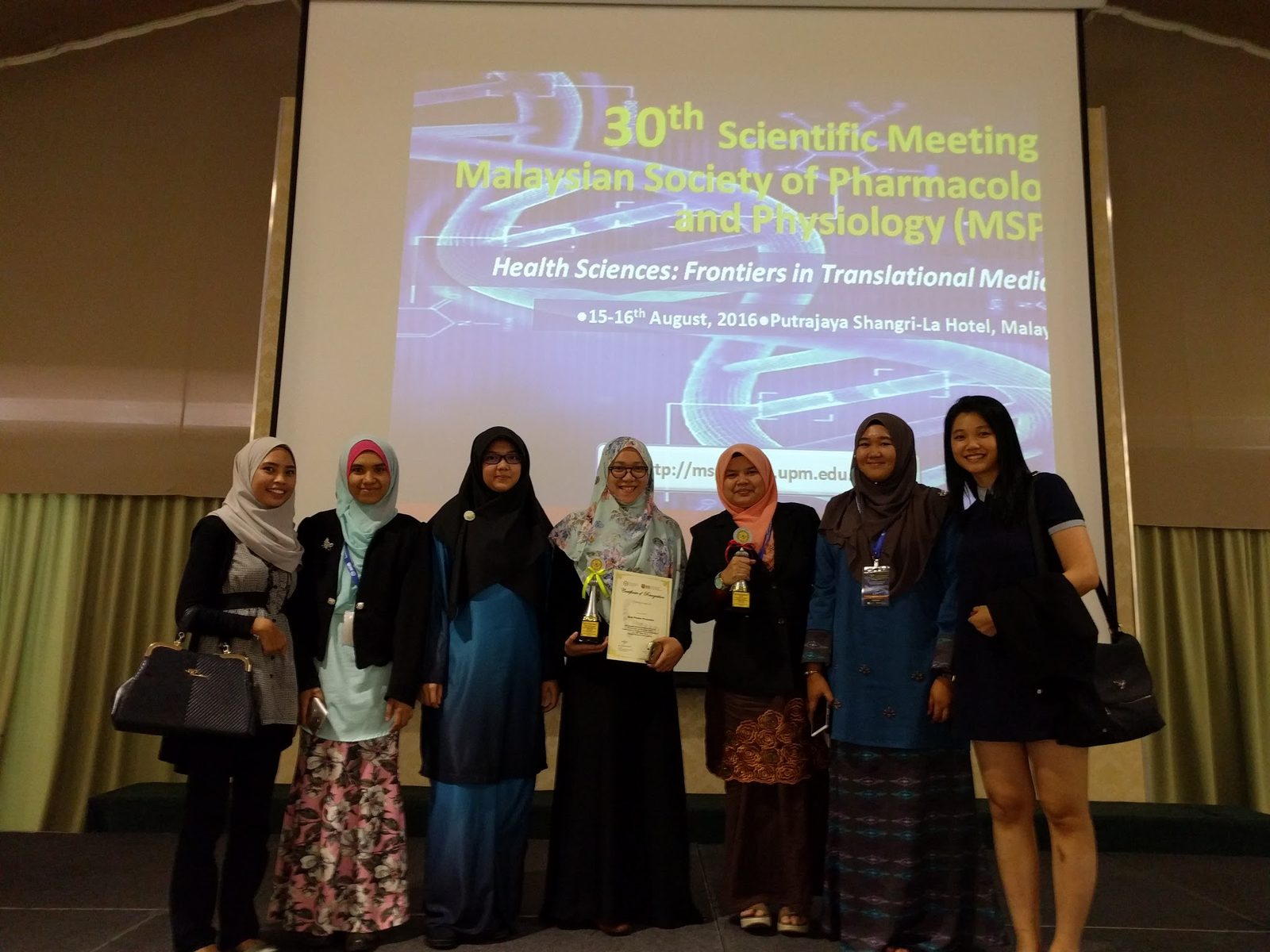 Seven delegates, two holding trophies, in front of the 30th MSPP Scientific Meeting title screen