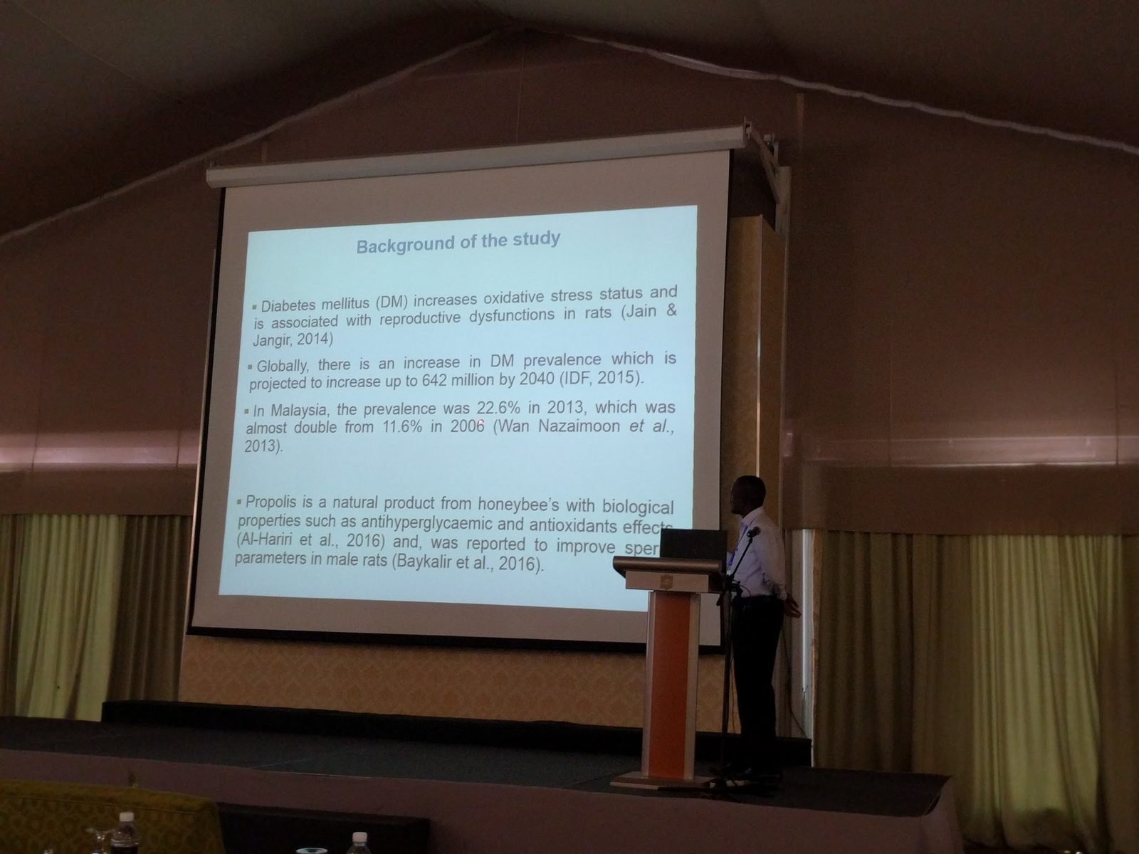 A presenter at the lectern beside a slide on diabetes and propolis in rats