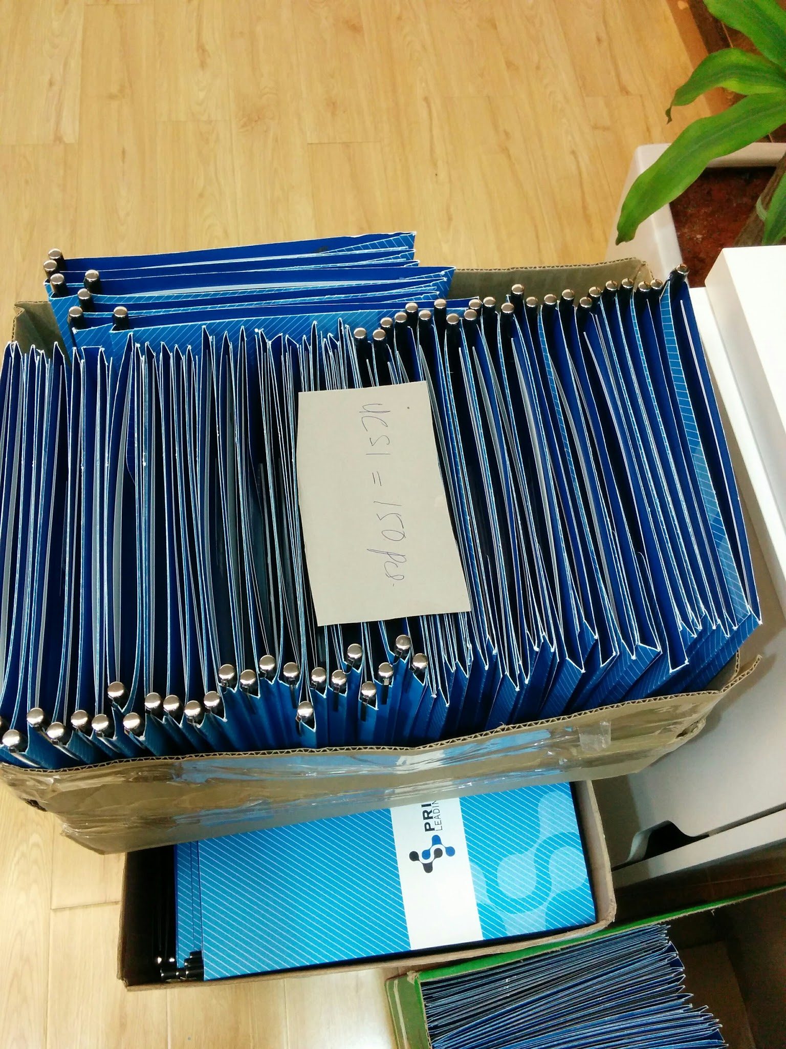 A box of blue Prima Nexus folders, packed and labelled for delivery, with a Prima Nexus branded box beneath
