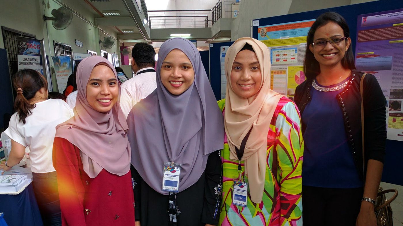 Four smiling delegates wearing seminar name tags stand together in front of research posters
