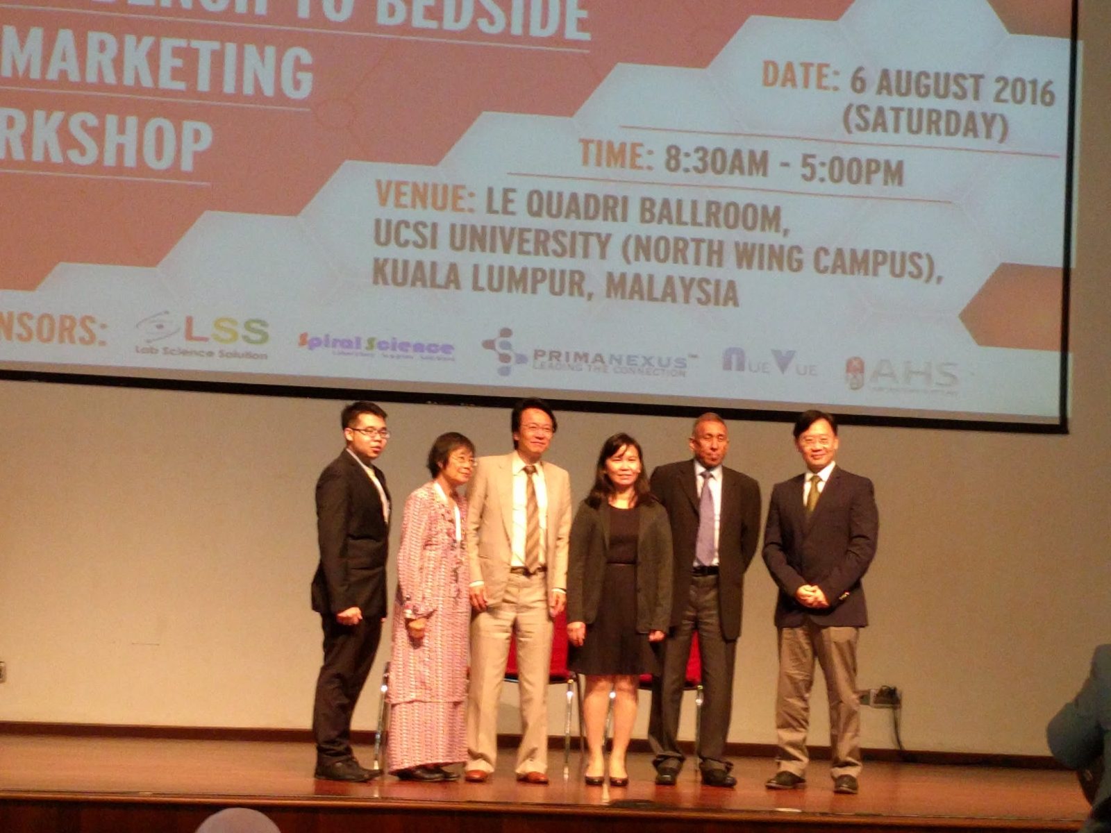 Six people standing in a row on stage under the workshop slide showing the date, venue and sponsors