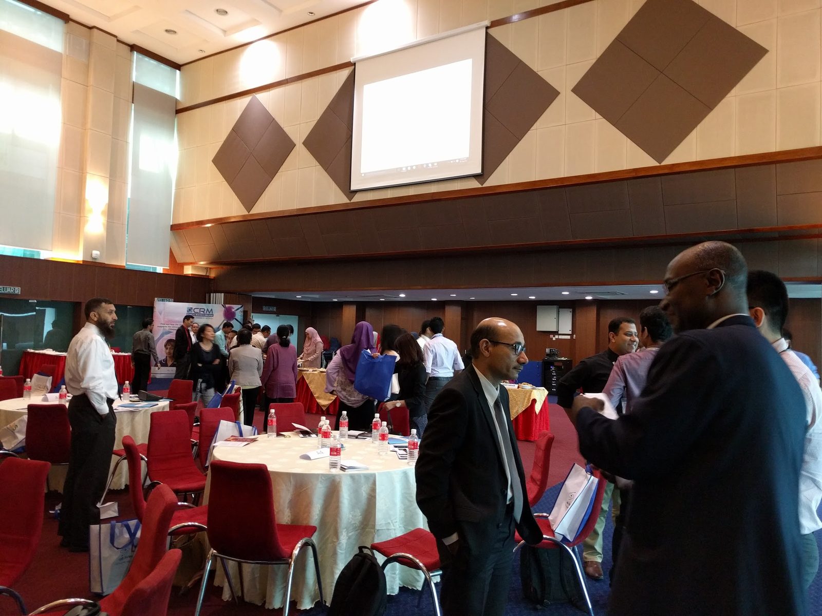 Participants standing and talking between round tables in the ballroom, with a refreshment table at the back