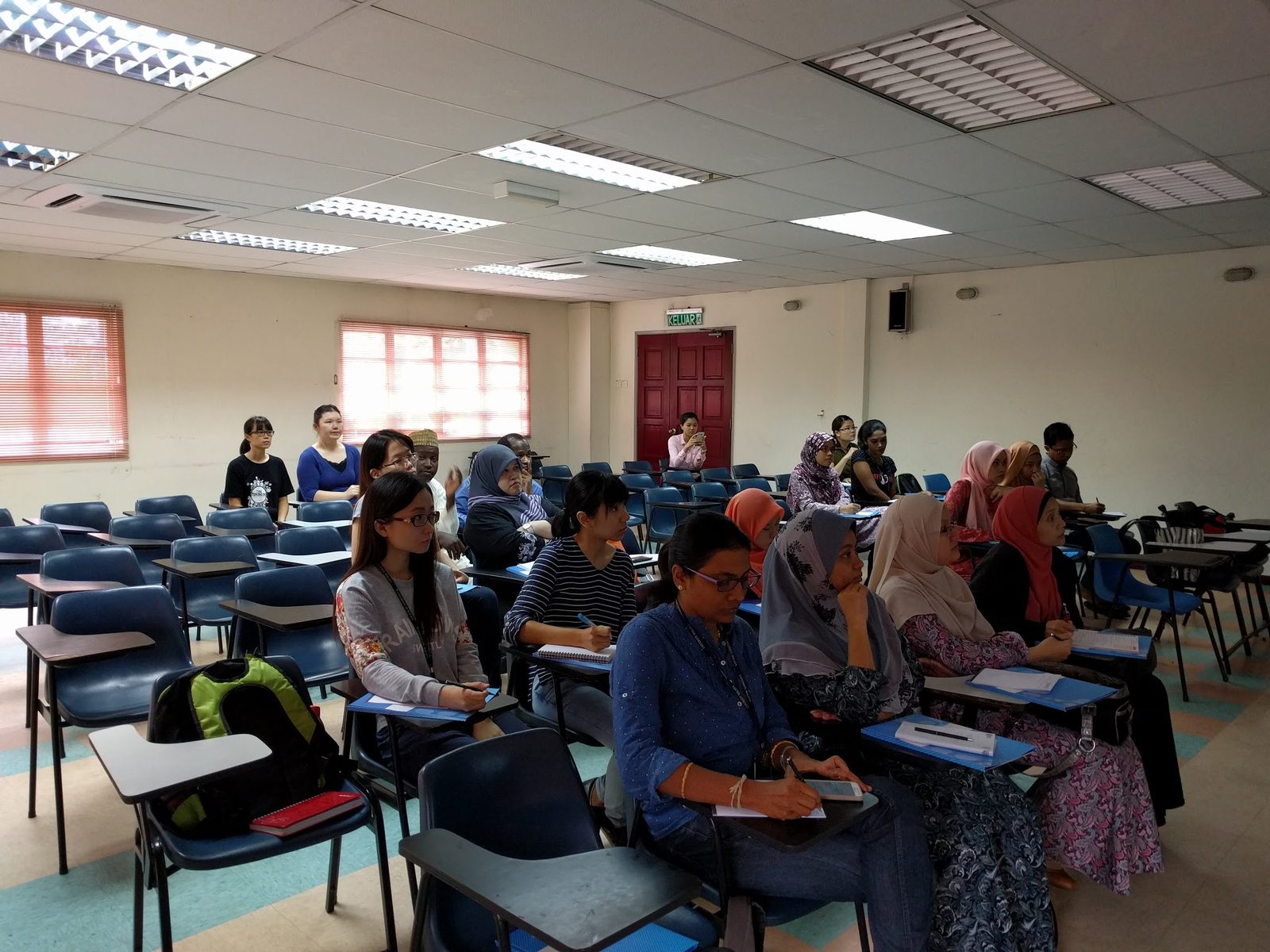 Participants seated at desks in a bright seminar room, some taking notes, during the workshop.