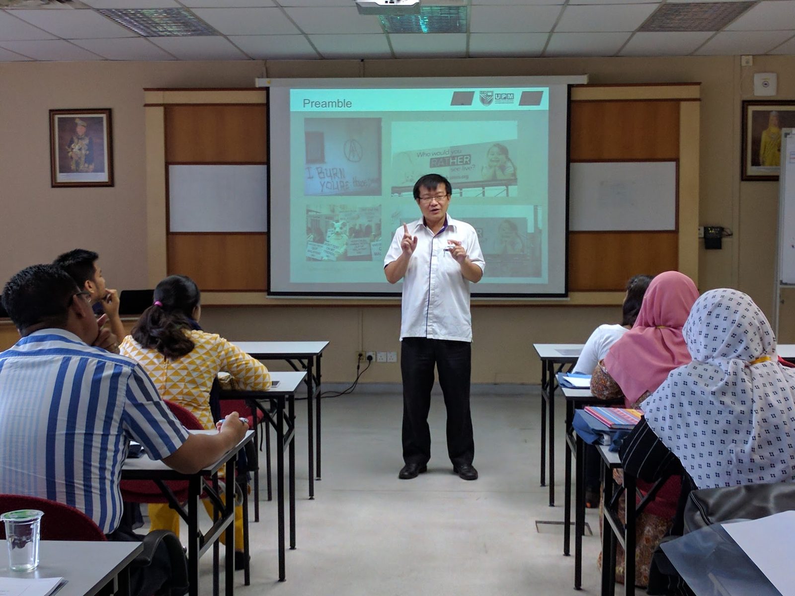 A speaker presents to seated participants in front of a projected slide