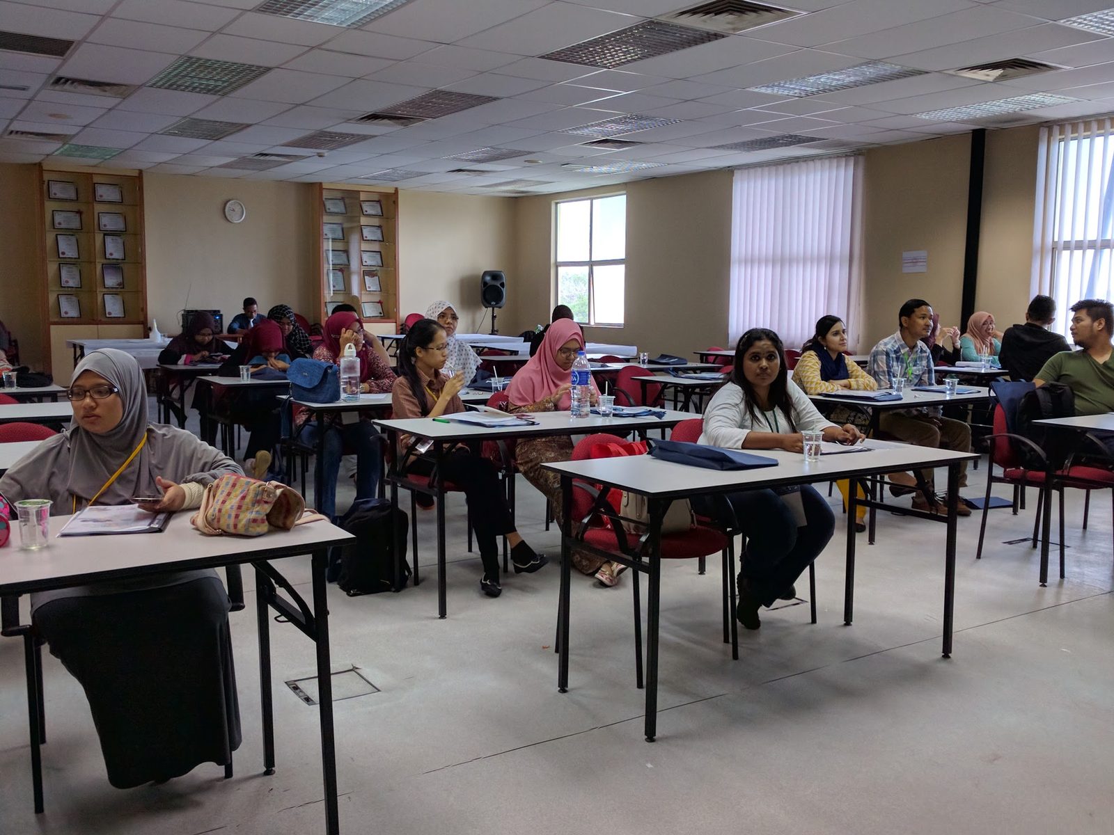 Participants seated at desks in the lecture room, with folders and drinks on the desks