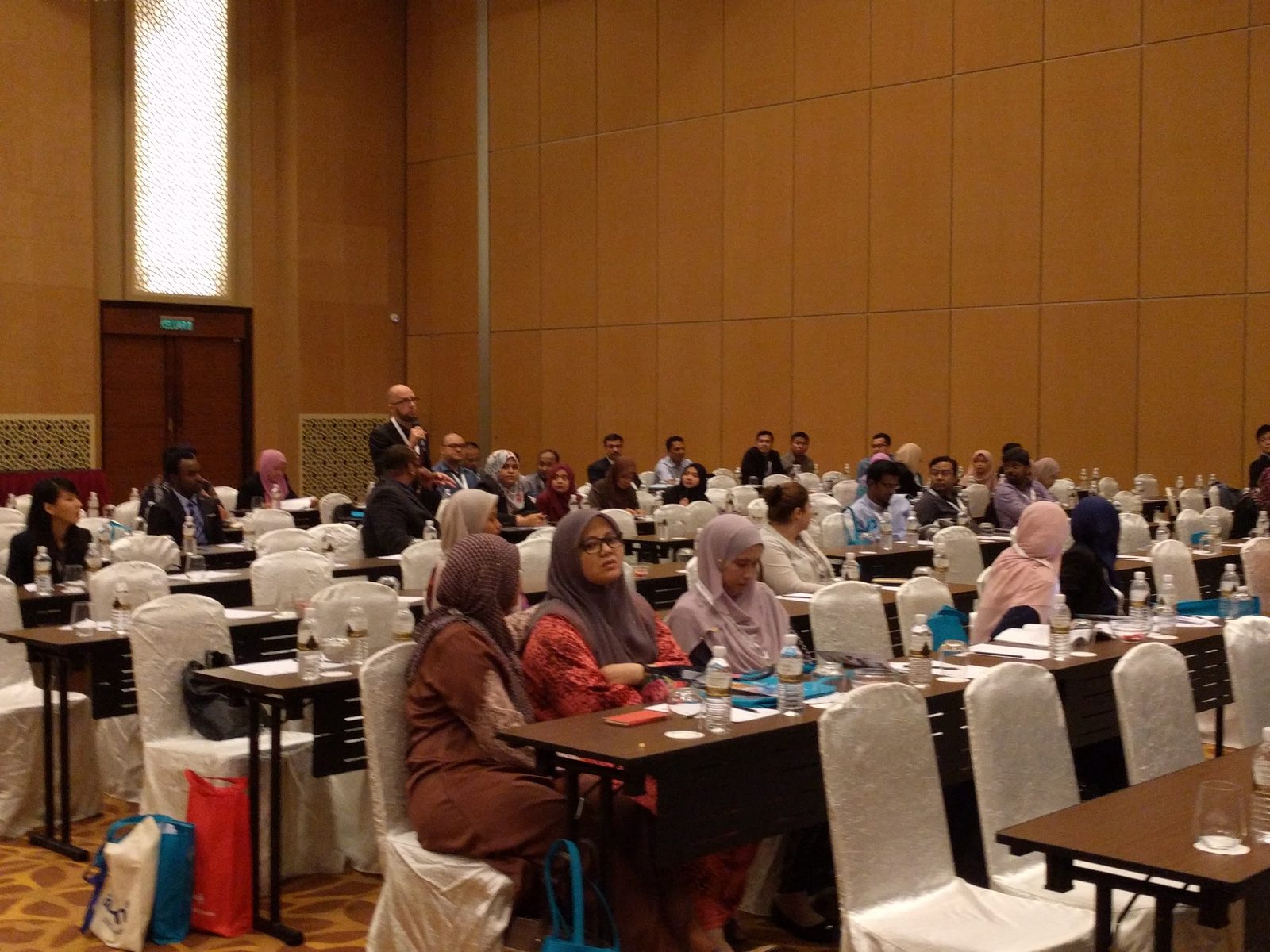 A delegate stands with a microphone to ask a question, with seated delegates around him