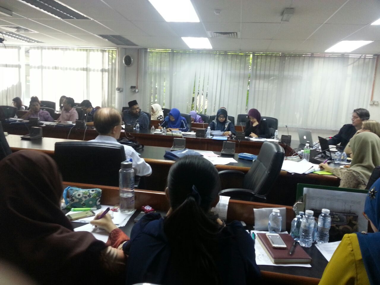 Participants taking notes at long desks with laptops and notebooks during a workshop session