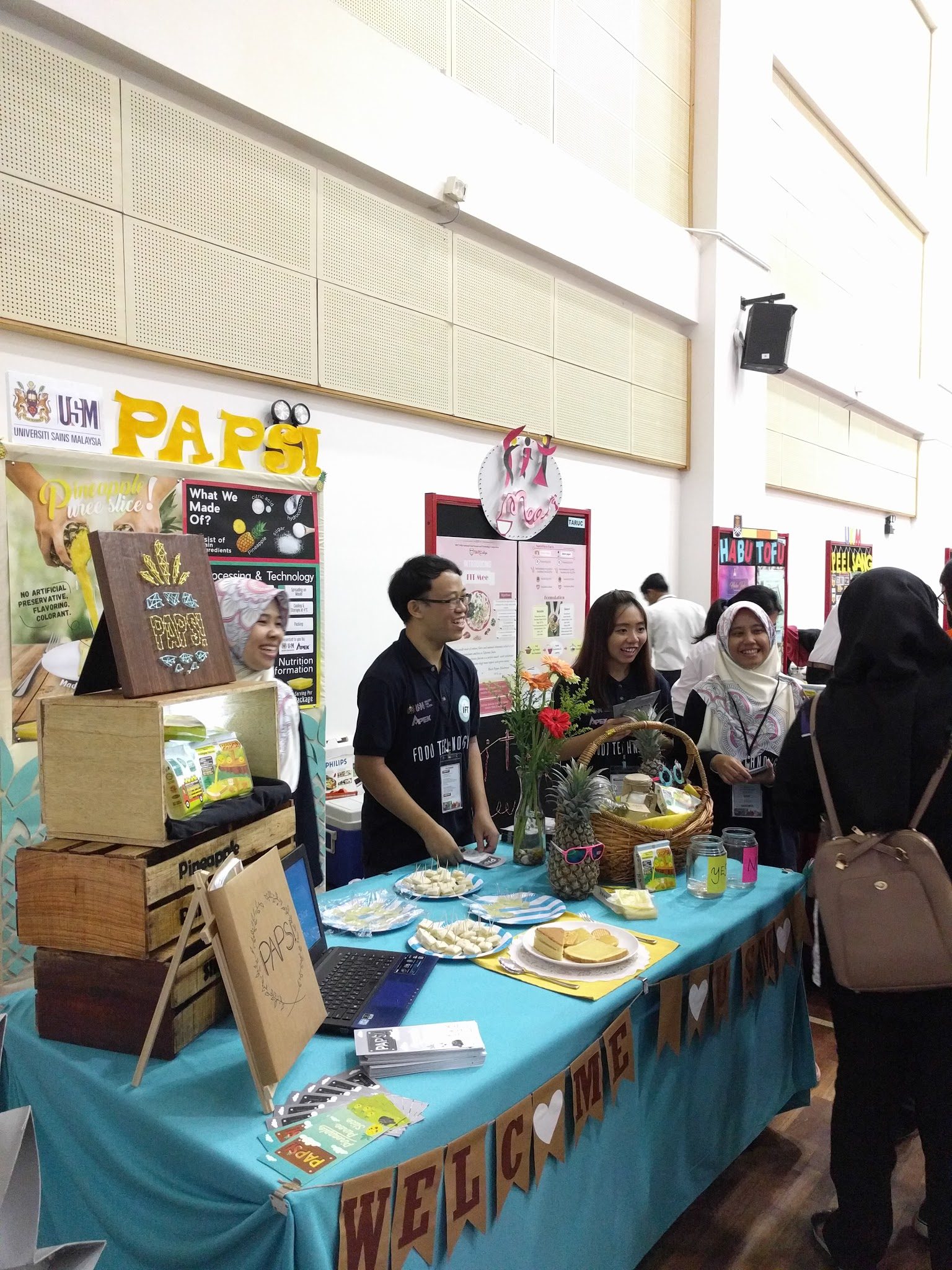 Students at a decorated food product booth talk with visitors in the hall