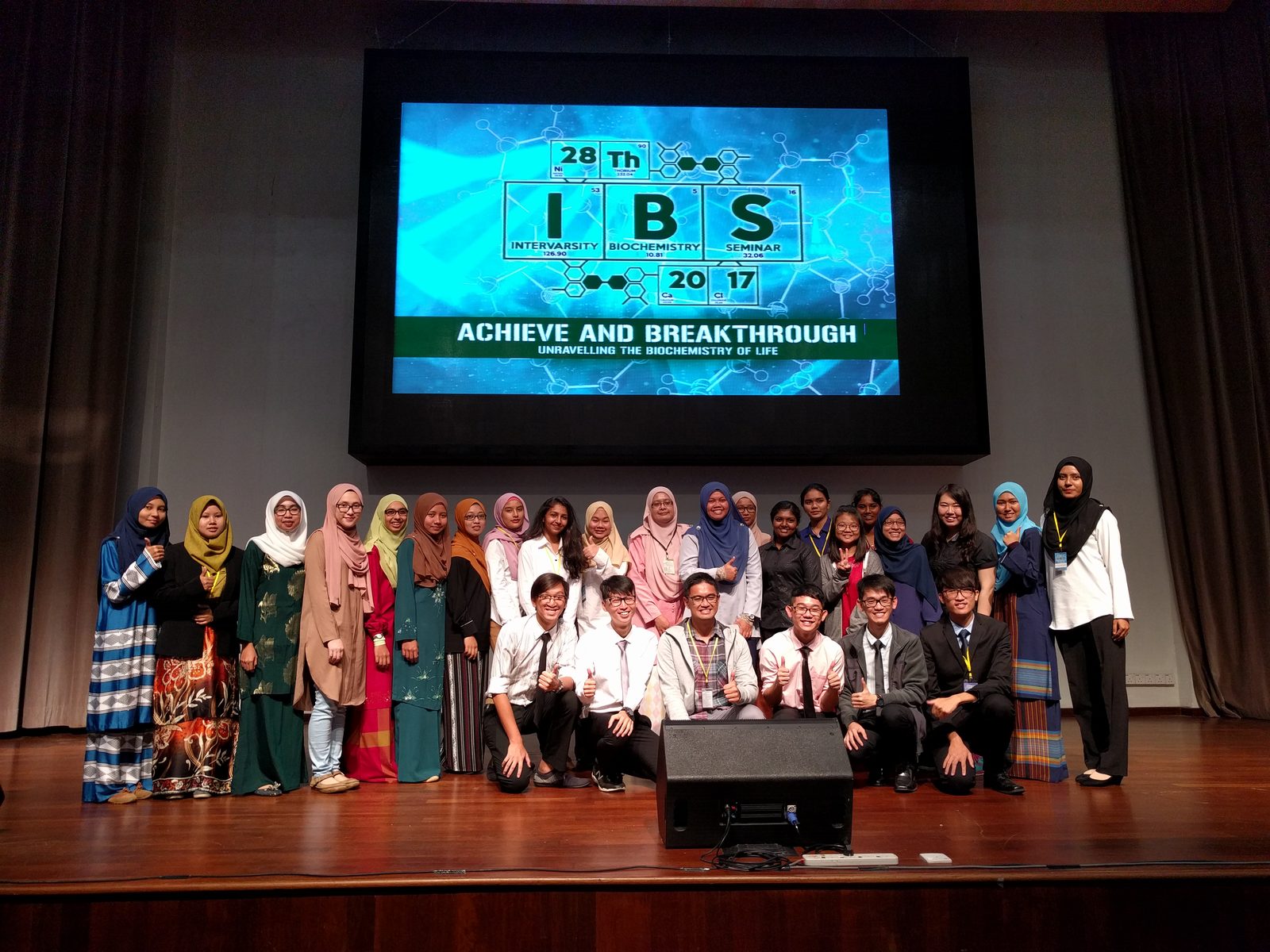 Participants pose for a group photo on stage under a large screen showing the IBS 2017 seminar logo
