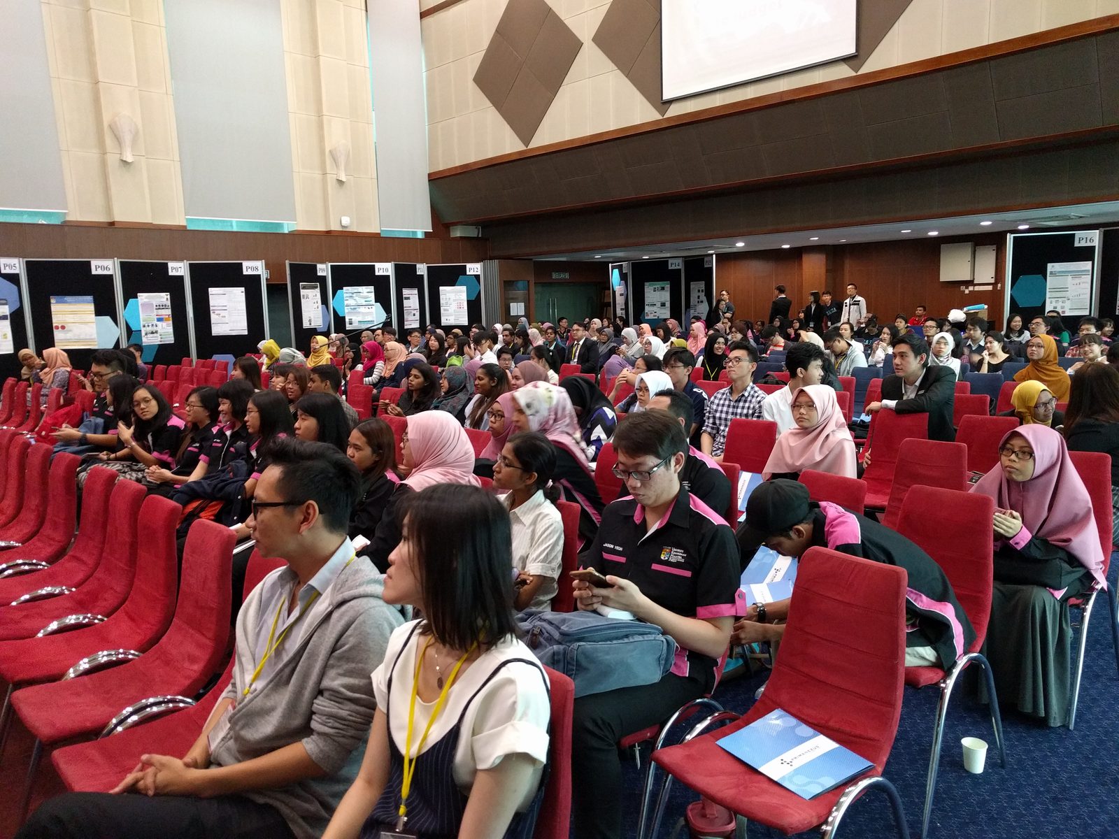 Seated audience in the ballroom, with poster boards behind them and blue Prima Nexus folders on the chairs
