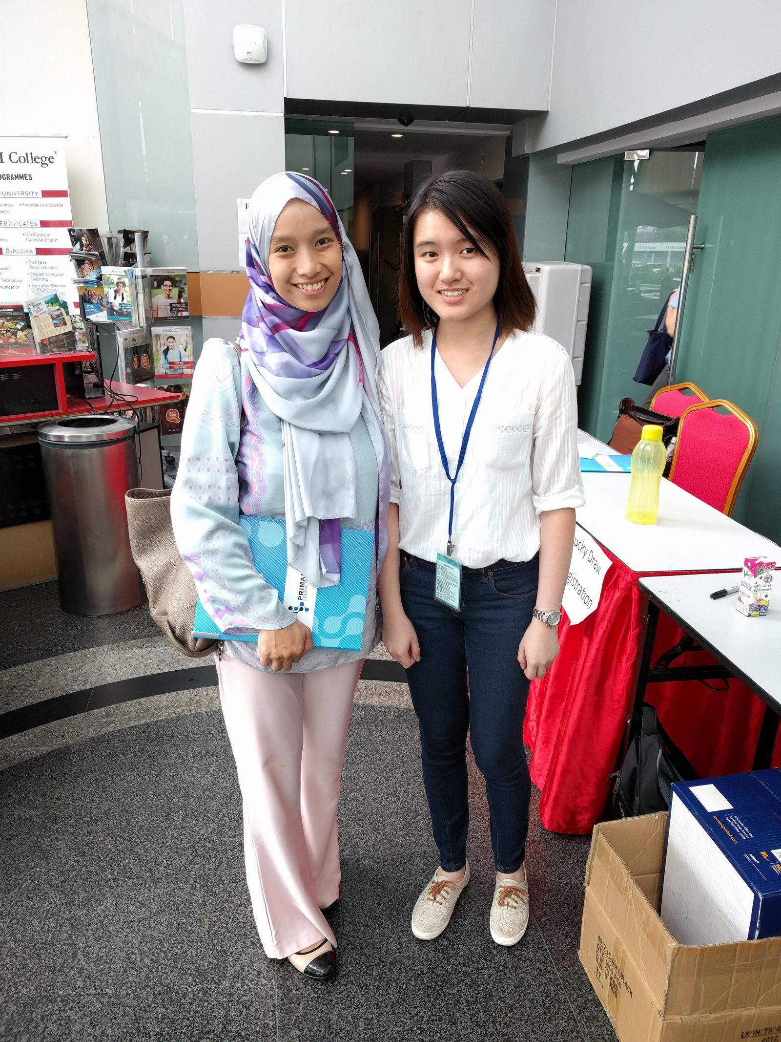 Two participants in the foyer, one holding a blue Prima Nexus folder