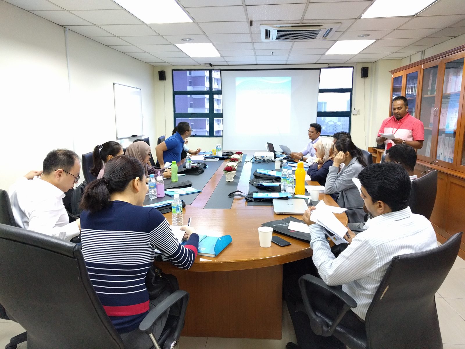Participants seated around a long table in a meeting room, with a presentation on the screen