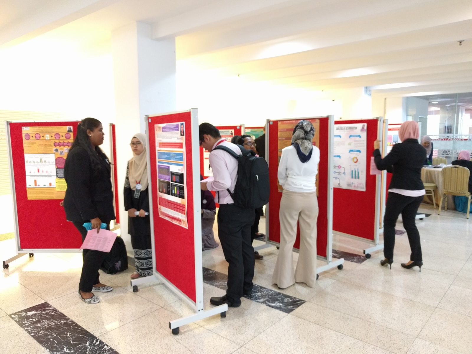 Students in formal dress reading research posters on red display boards in the foyer
