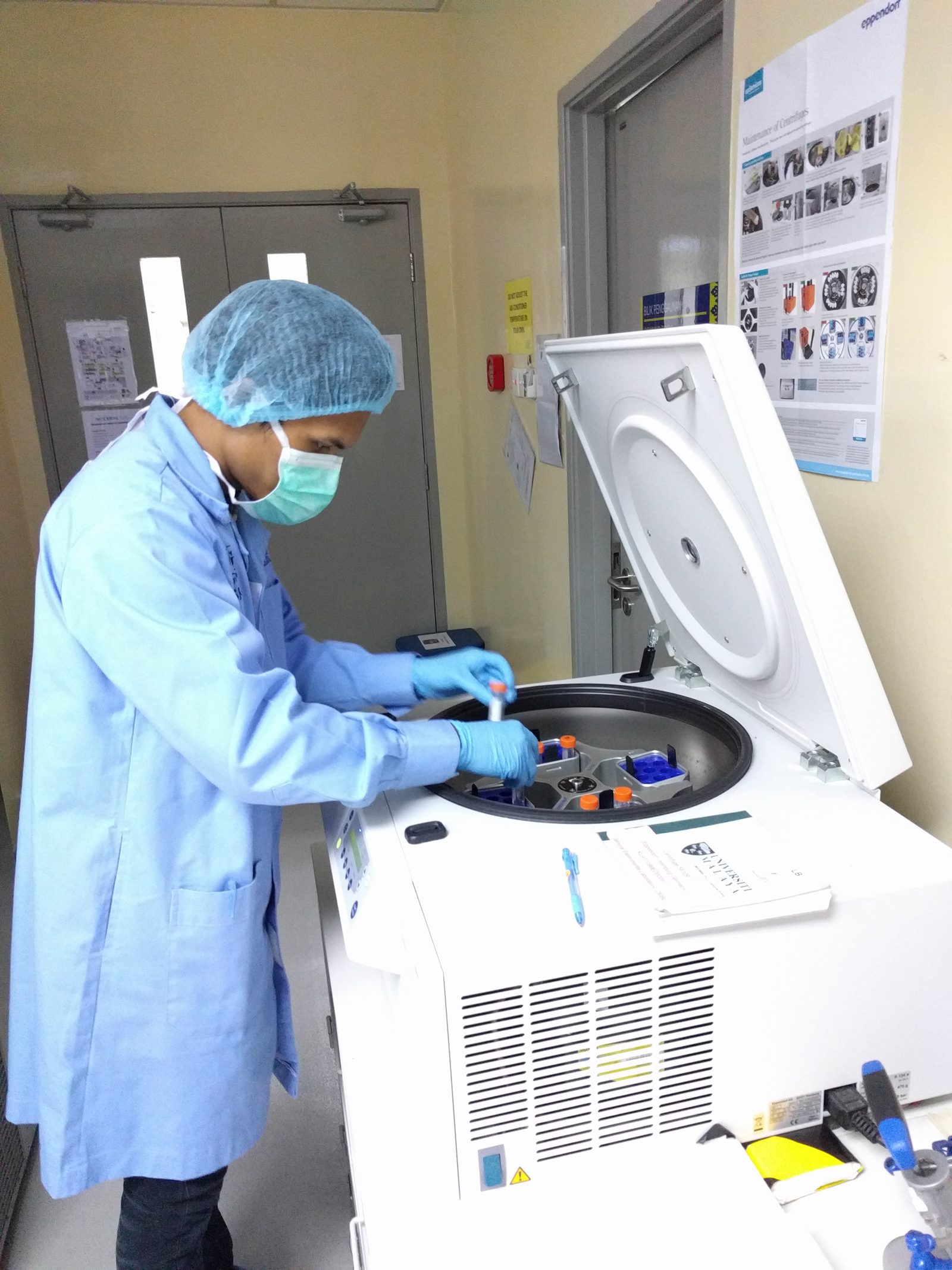 A participant in a lab coat loads sample tubes into a benchtop centrifuge