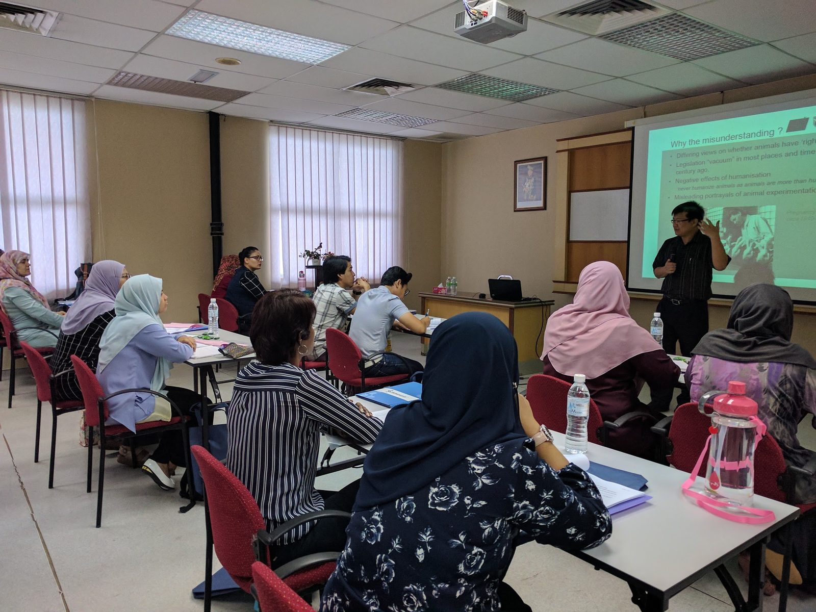A speaker presents slides to participants seated at tables in the workshop room