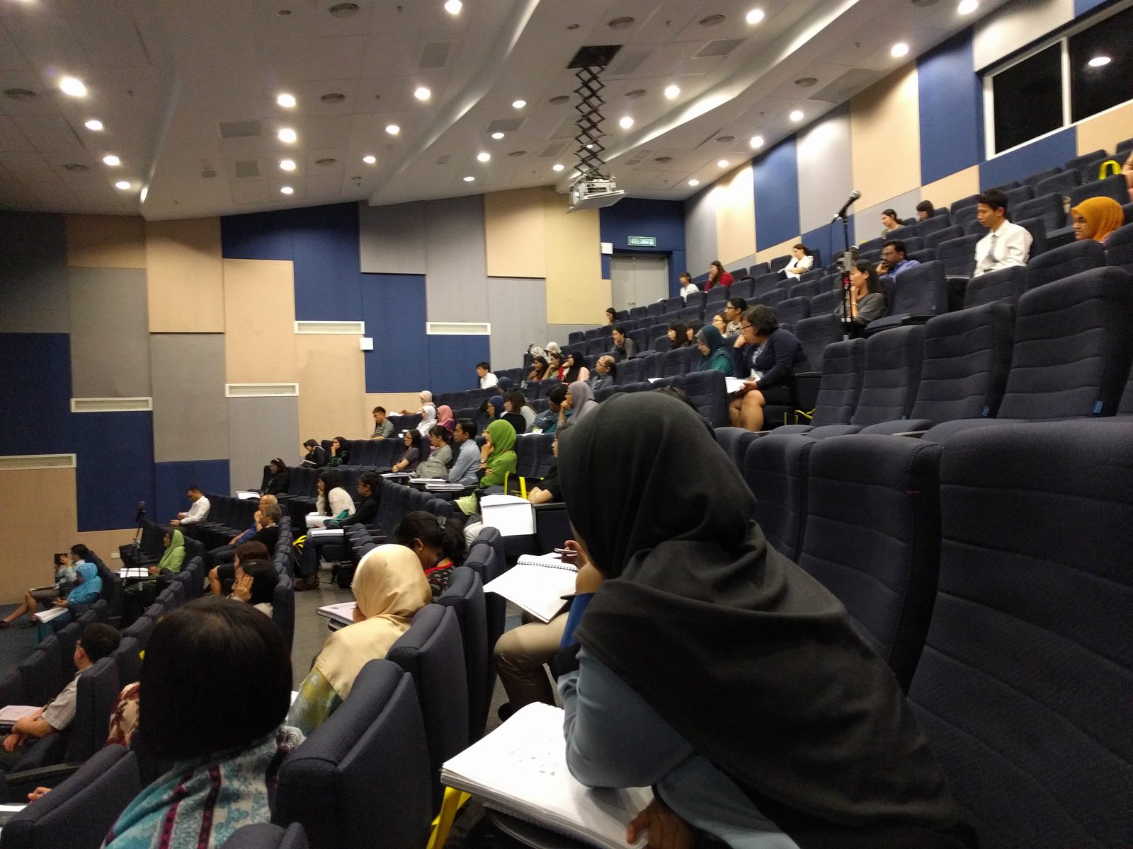 Delegates seated across the tiered auditorium with notes on their laps during a session