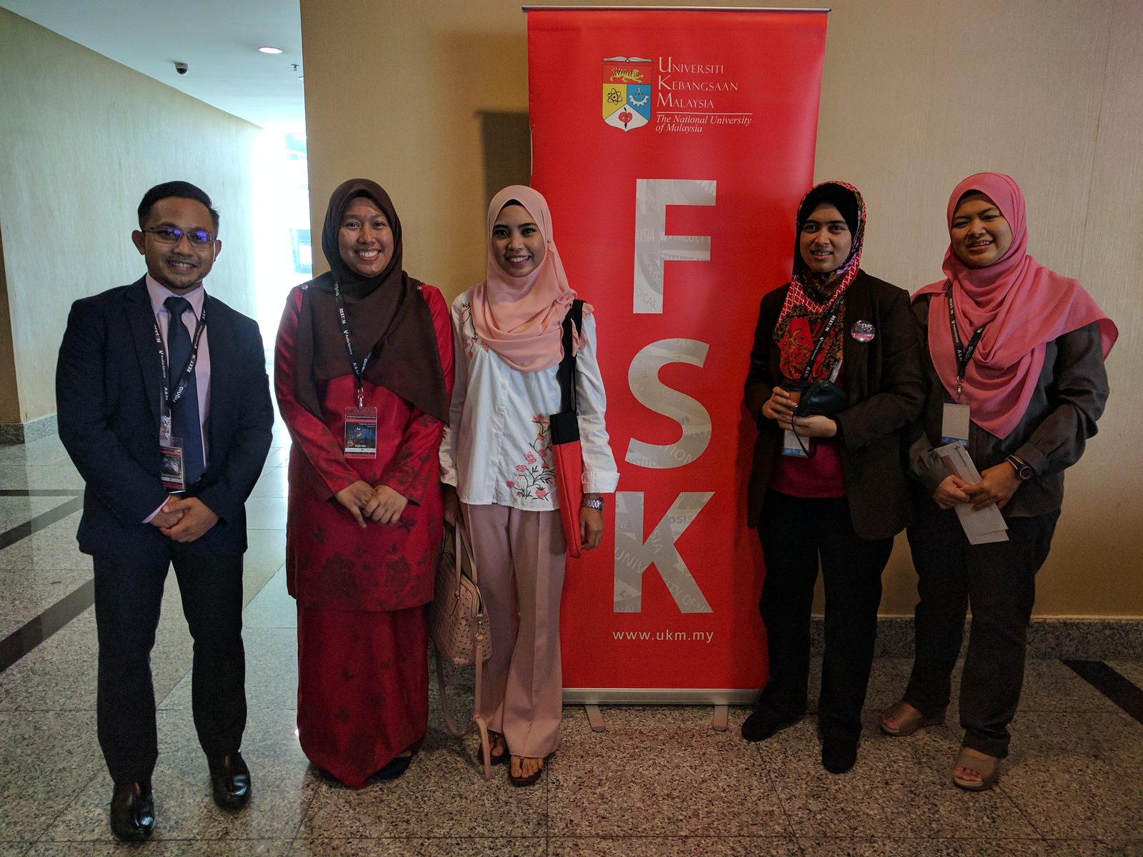 Five people wearing lanyards stand beside a red UKM Faculty of Health Sciences (FSK) banner