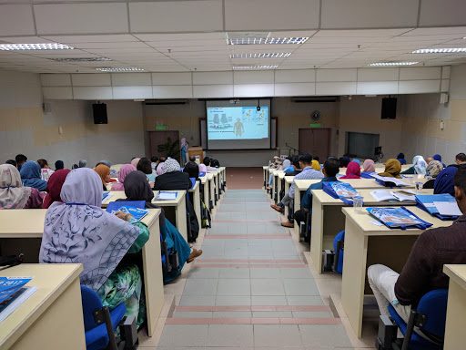A full lecture hall of delegates facing a projected slide during a talk.