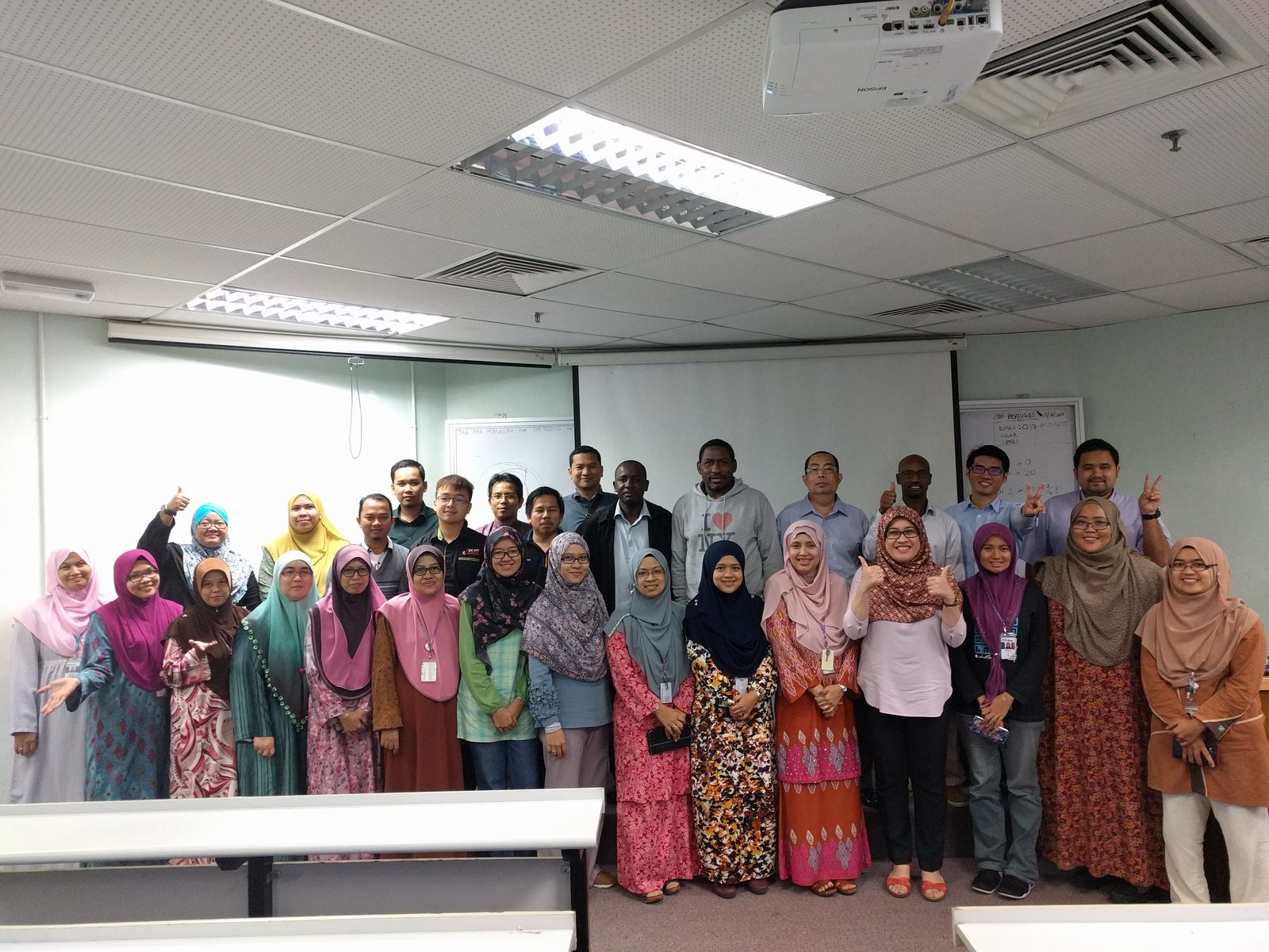 Group photo of the workshop participants standing in rows in front of the screen in a lecture room