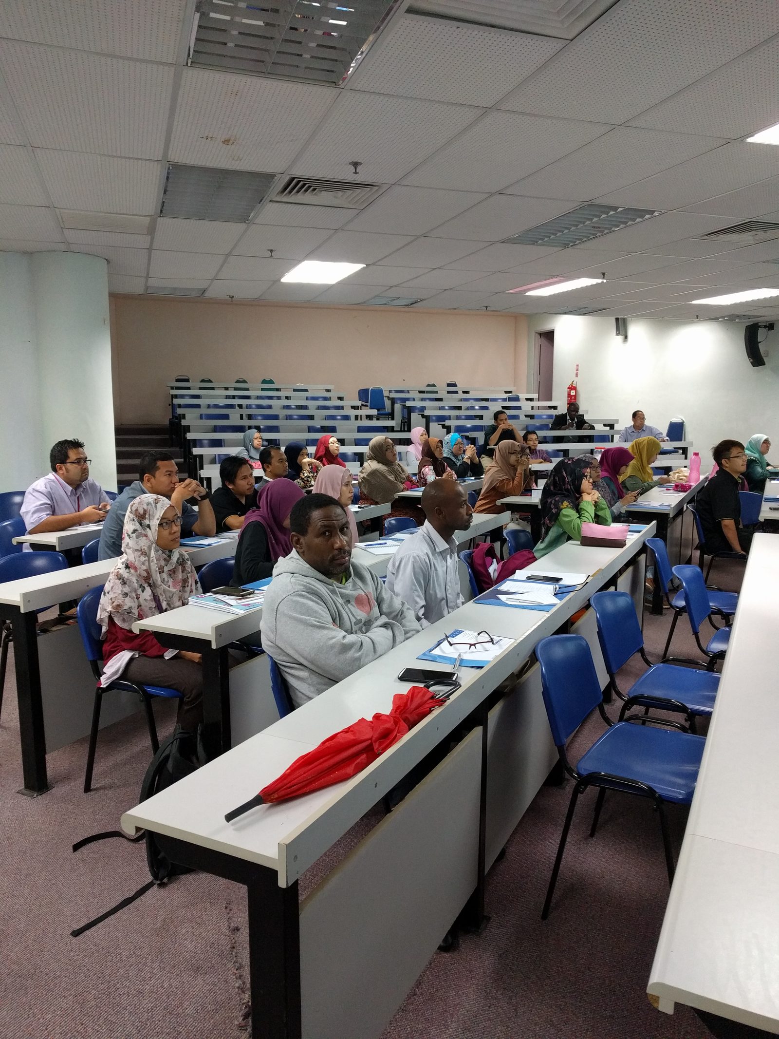 Participants at their desks with workshop folders and notes, listening to a session