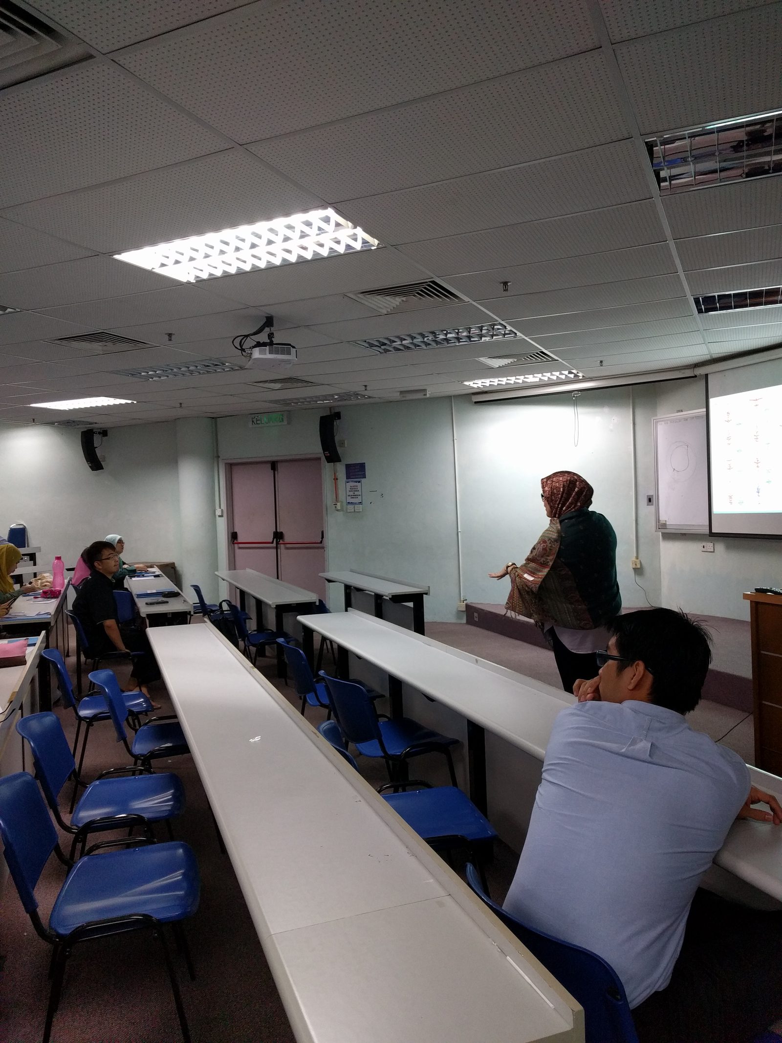 A presenter in a headscarf speaks to participants from the front of the lecture room
