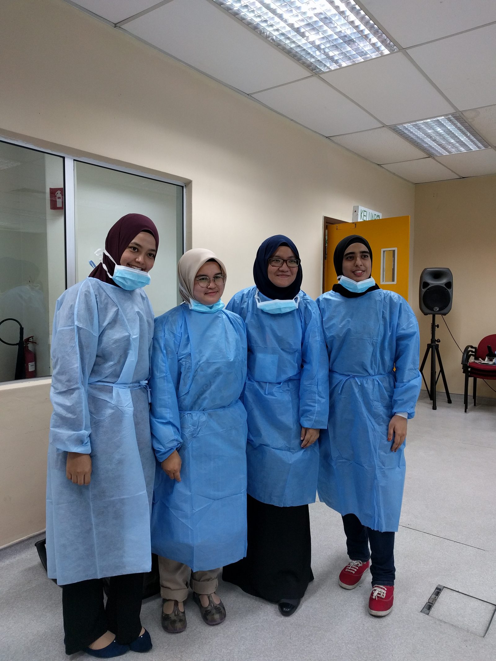 Four participants in blue gowns stand together for a photo in the workshop room